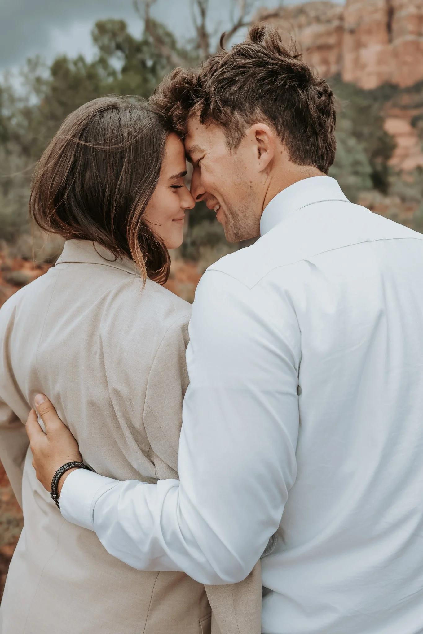A couple surrounded by Sedona red rock with their foreheads touching and eyes closed, smiling softly in an intimate moment.