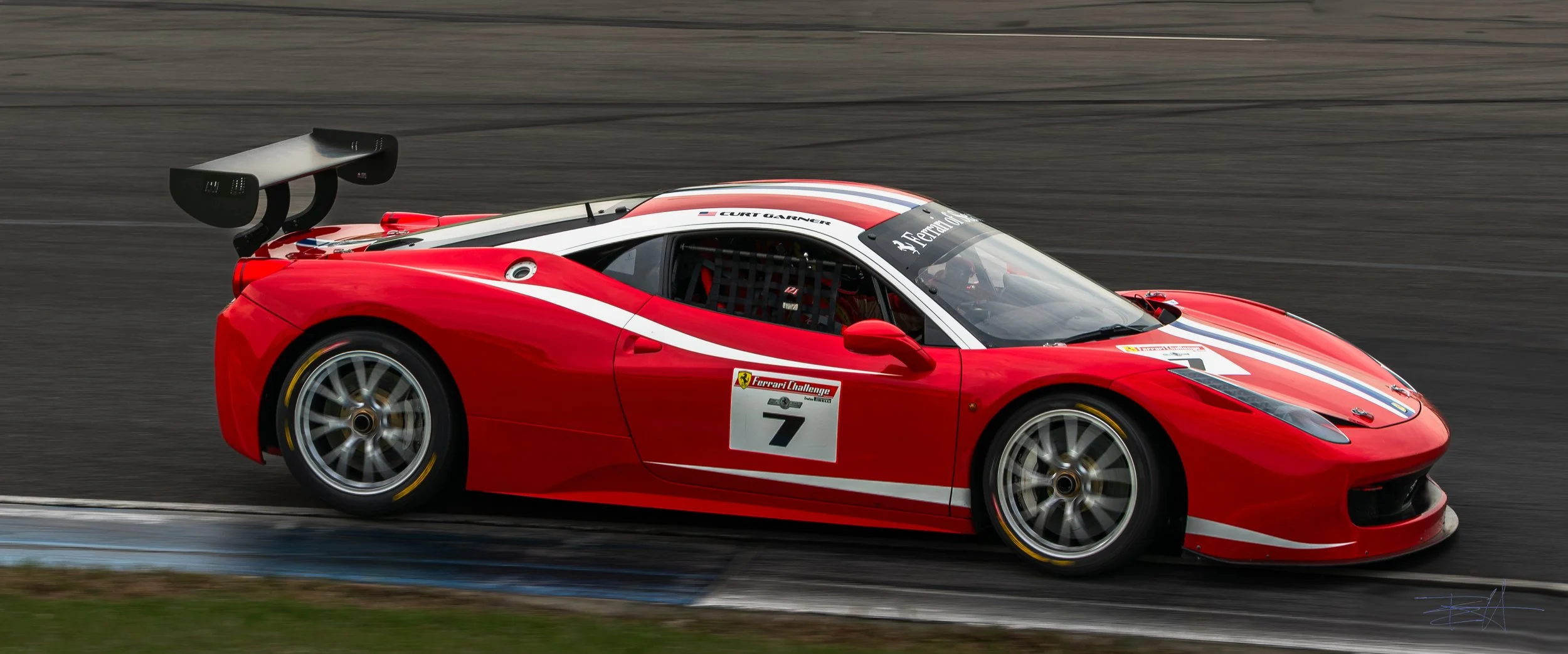 A red Ferrari 458 Challenge race car on a racetrack,, in motion.