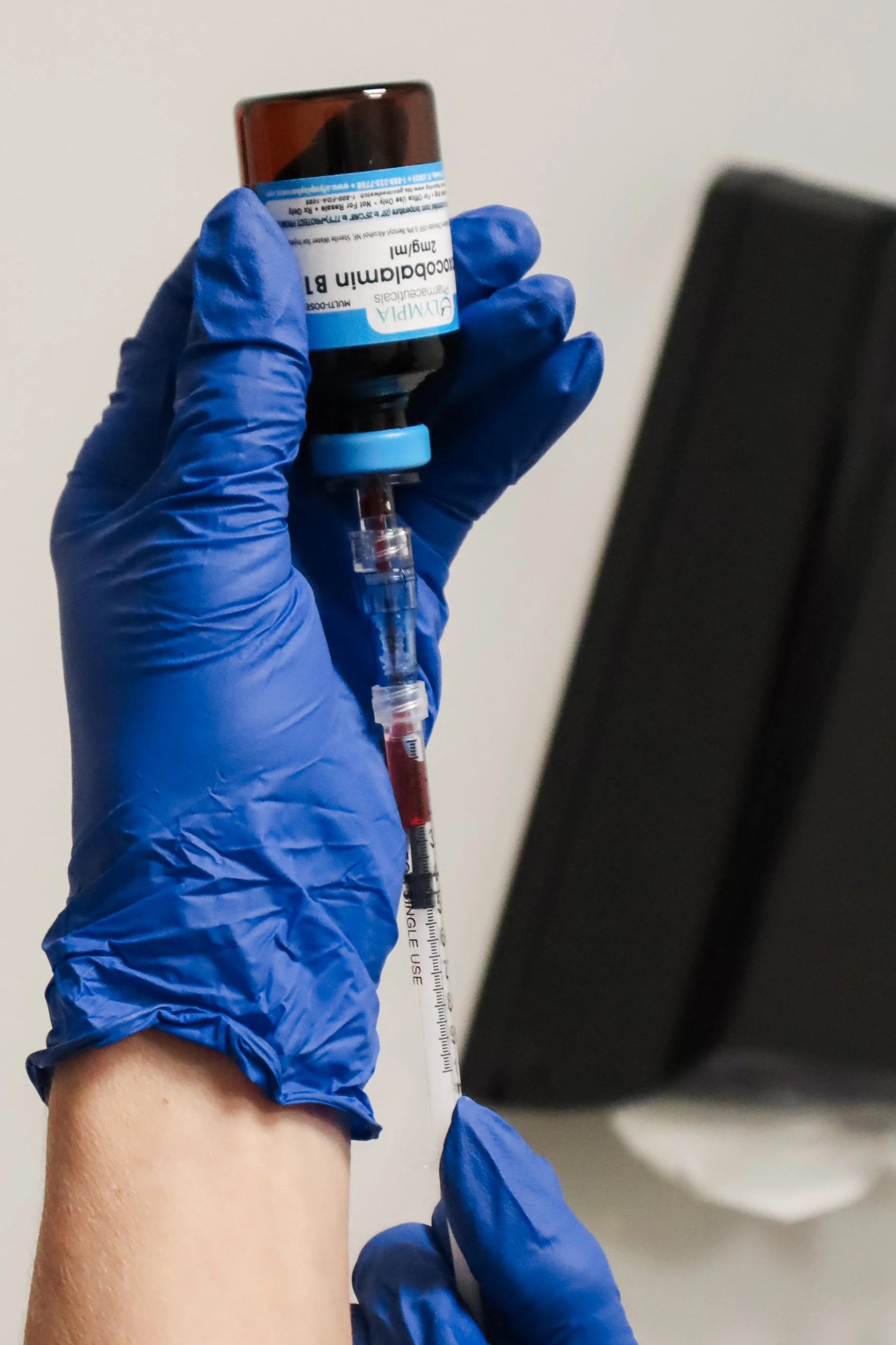 A person wearing blue gloves filling a syringe from a vial labeled 'COVID-19' for vaccination.