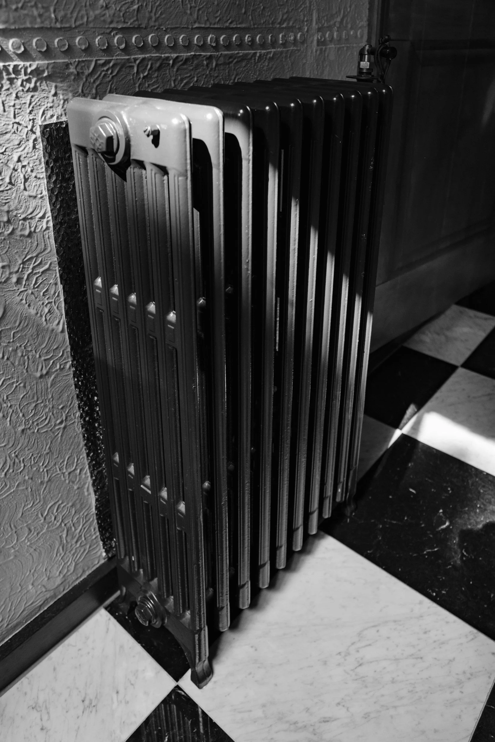 Black vintage radiator against textured wall with checkered tile floor.
