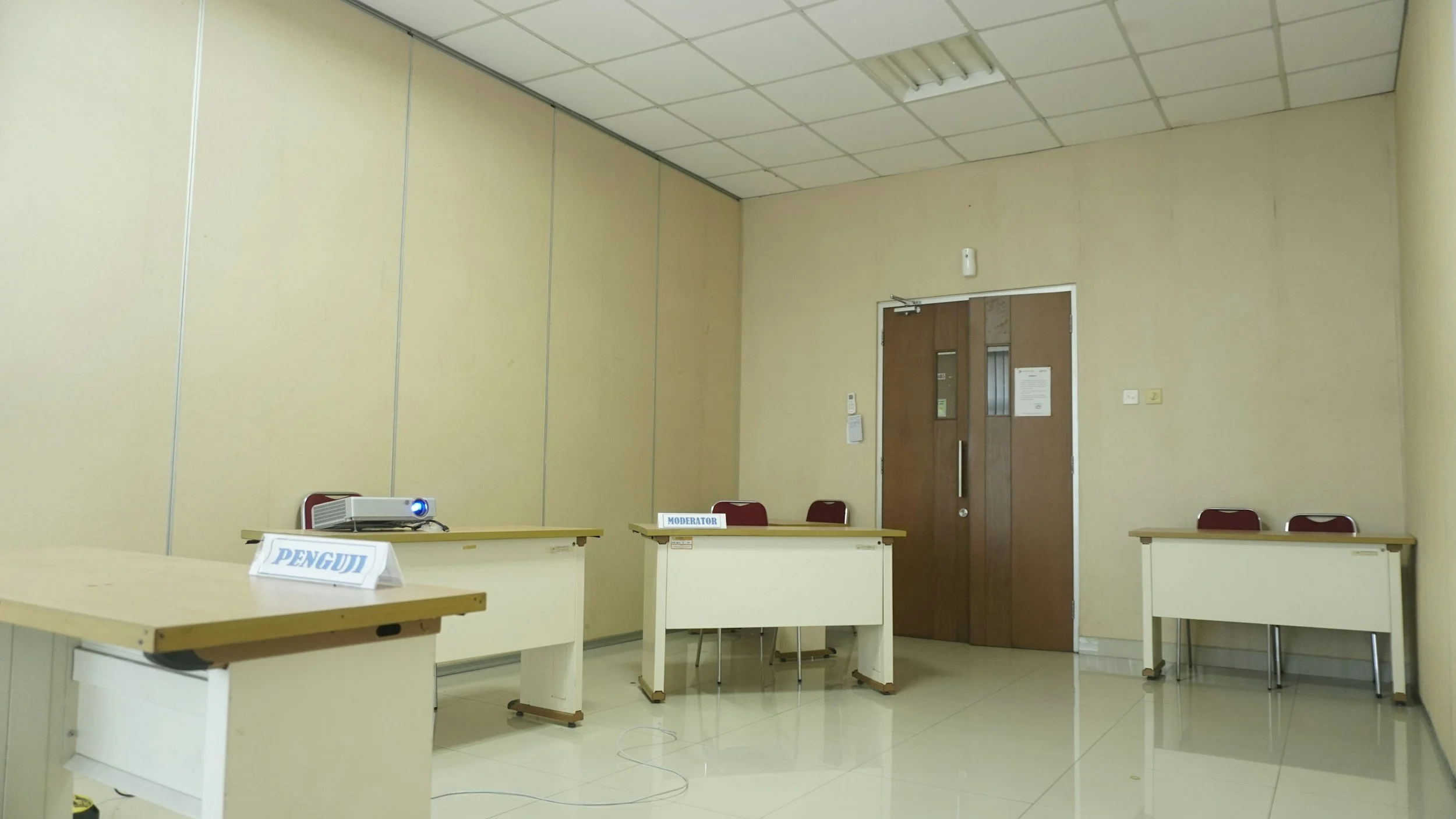Empty conference room with three tables, each with chairs, a projector on the left table, and signs labeled 'Penguin' and 'Moderator' on two of the tables.