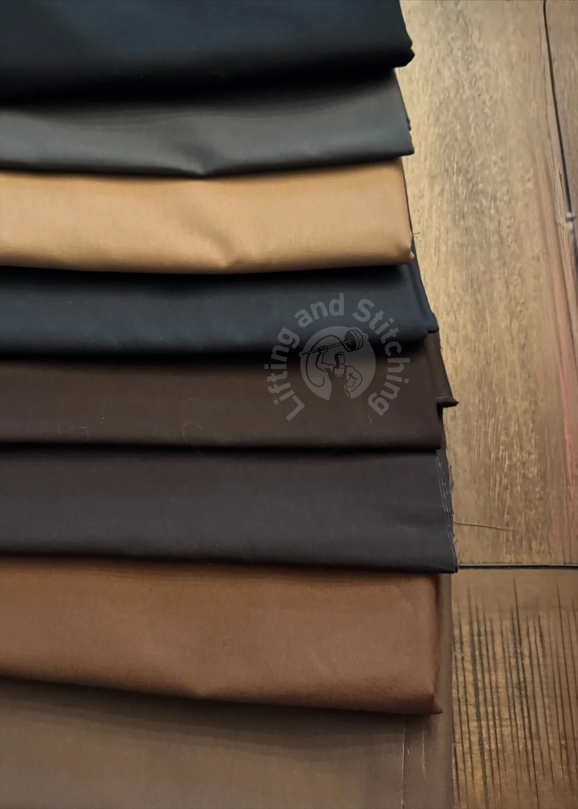 A close-up photo of eight fabrics cascading across a table. The fabrics are solid tones in various shades of browns and grays.