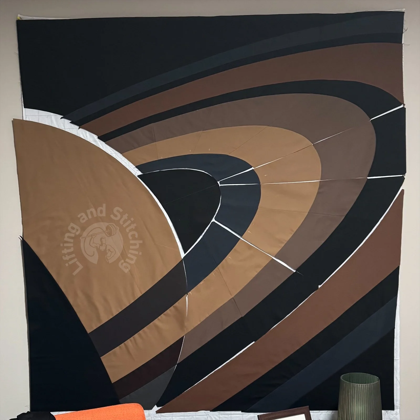 A quilt top nearly finished. The quilt is a large minimalistic design of the planet Saturn, depicting the rings and planet with shades of browns and grays for dimension, depth and transparency.