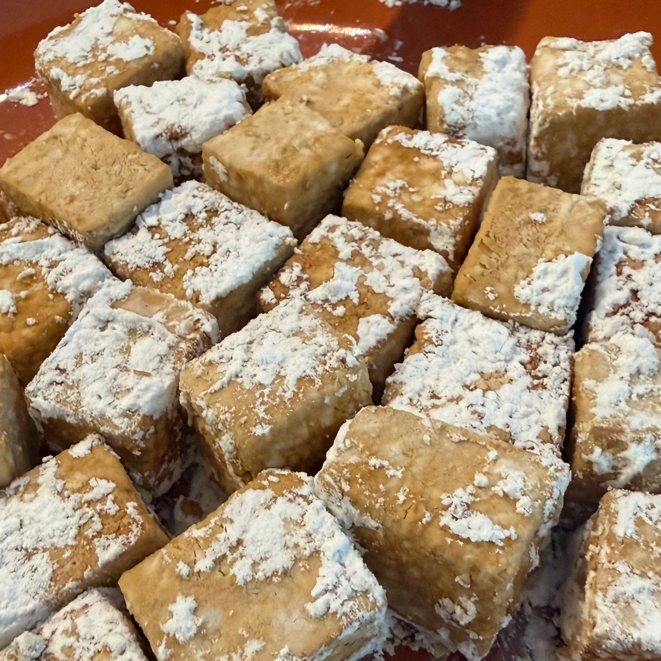 A close up photo of tofu that has been sliced into cubes, marinated and tossed in a tapioca starch. They are each laying in a single layer on a dinner plate, prepared for frying.