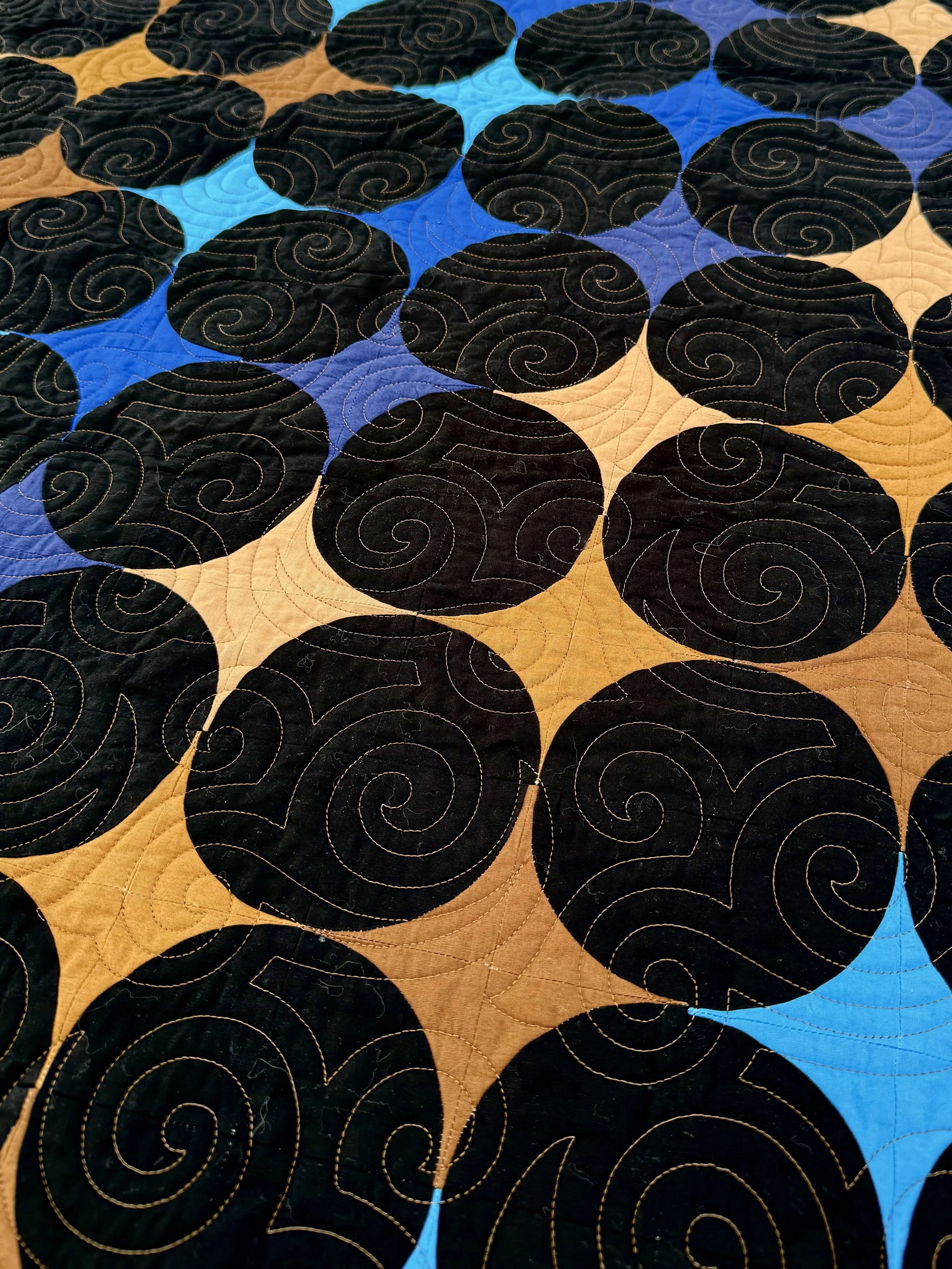 Close up of the quilting of a quilt titled A Trip Around the Universe with a flowing wave of brown and blue fabric arranged into retro-modern four-point stars.