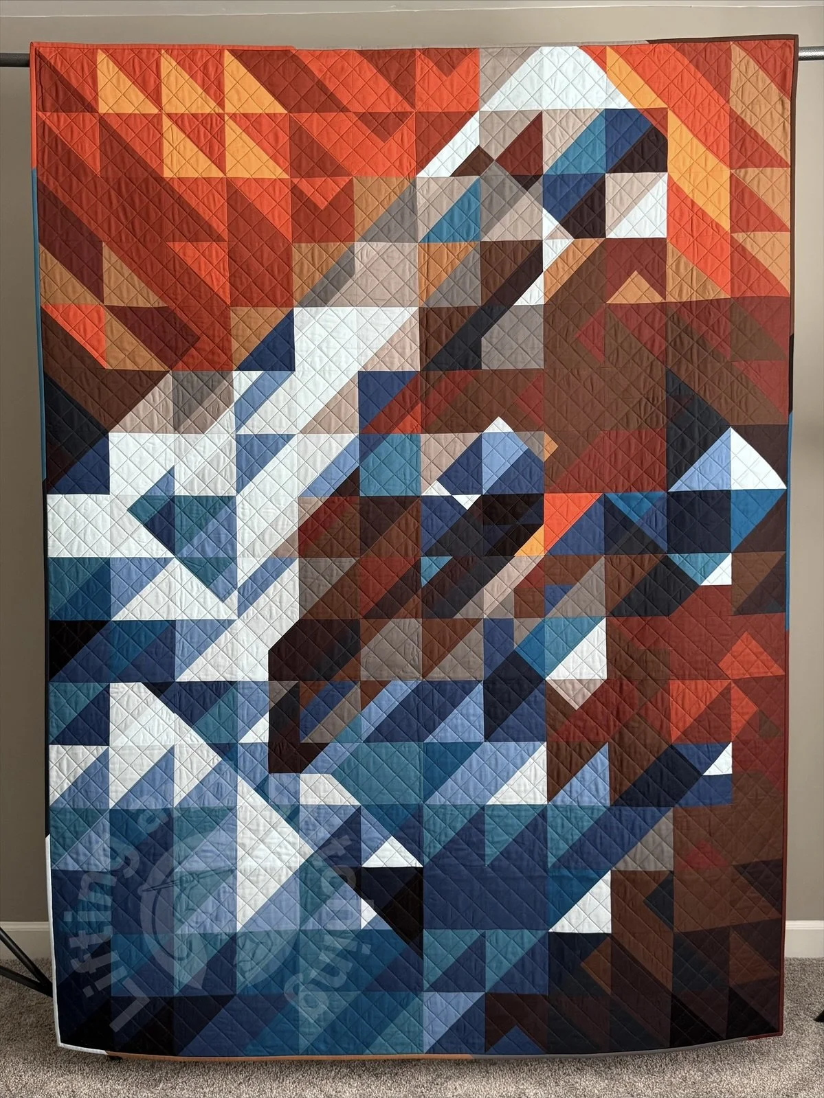 A full photograph of a quilt, an abstract of color and diagonal triangles organized to look like a nebula.