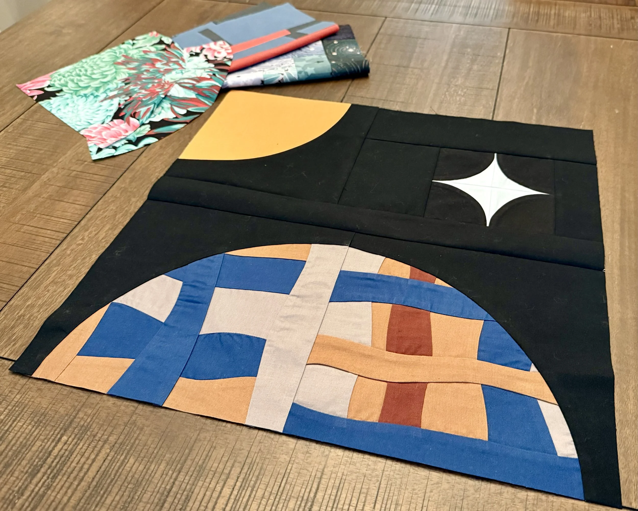 A finished block shows a retro style curve pieced block. A horizon view of a half circle made of improvisational piecing lays at the bottom. In the corner left is a quarter sun imitating a sun and on the right is a small four point star in ice blue.