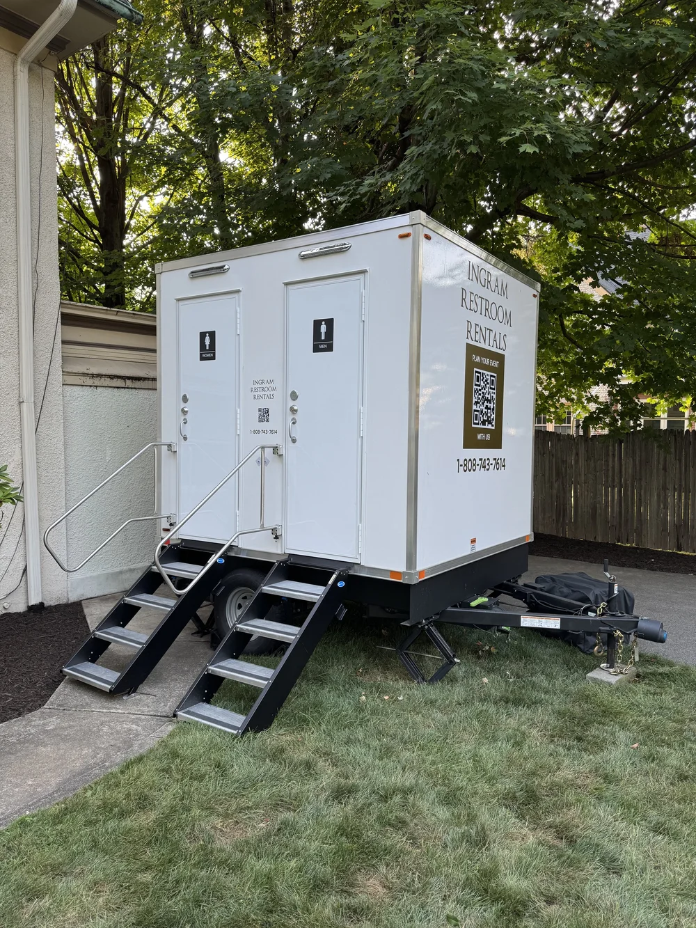 Restroom trailer with steps and handrails in a fenced backyard