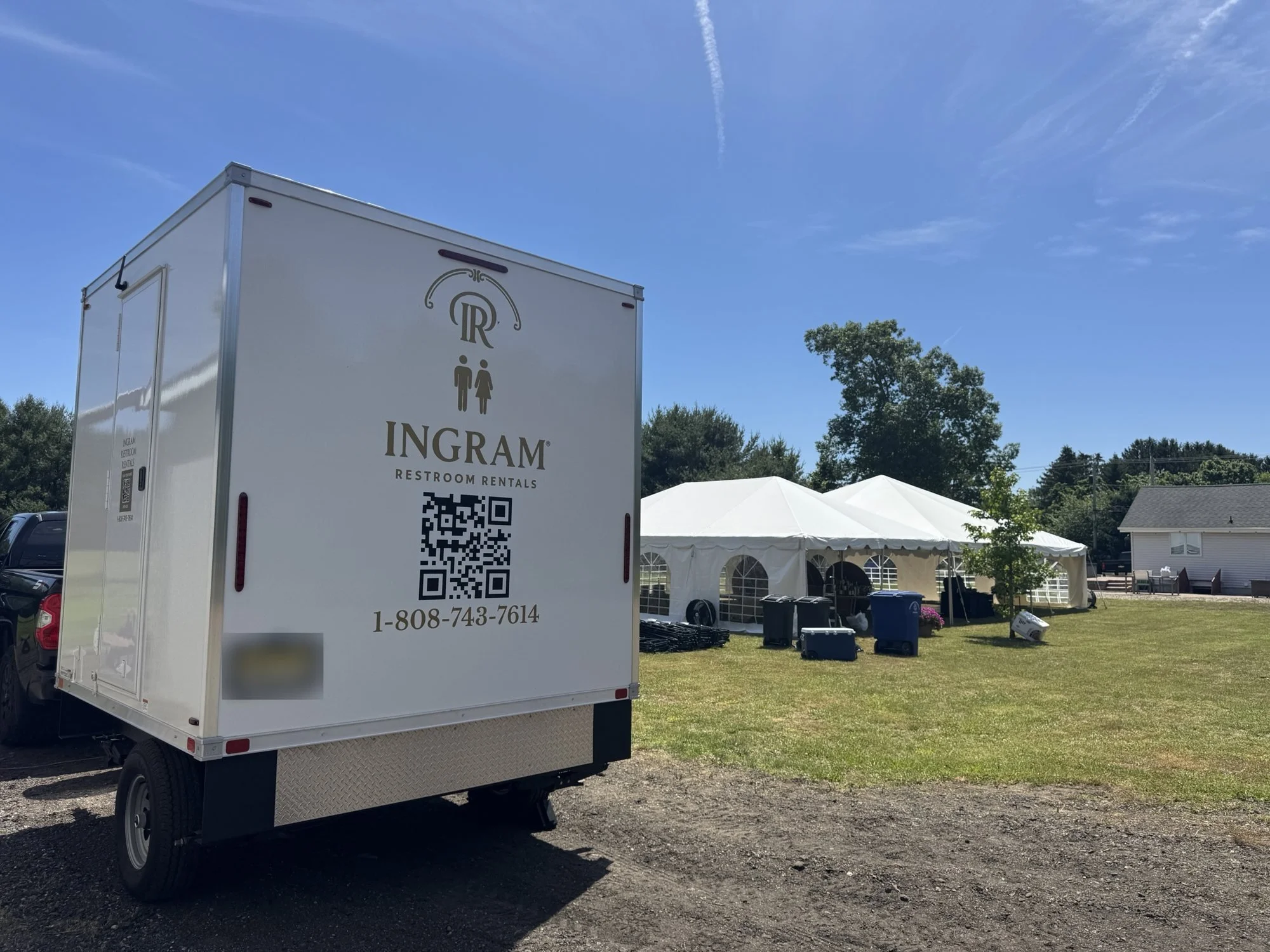An Ingram luxury restroom trailer set up on a field beside white event tents