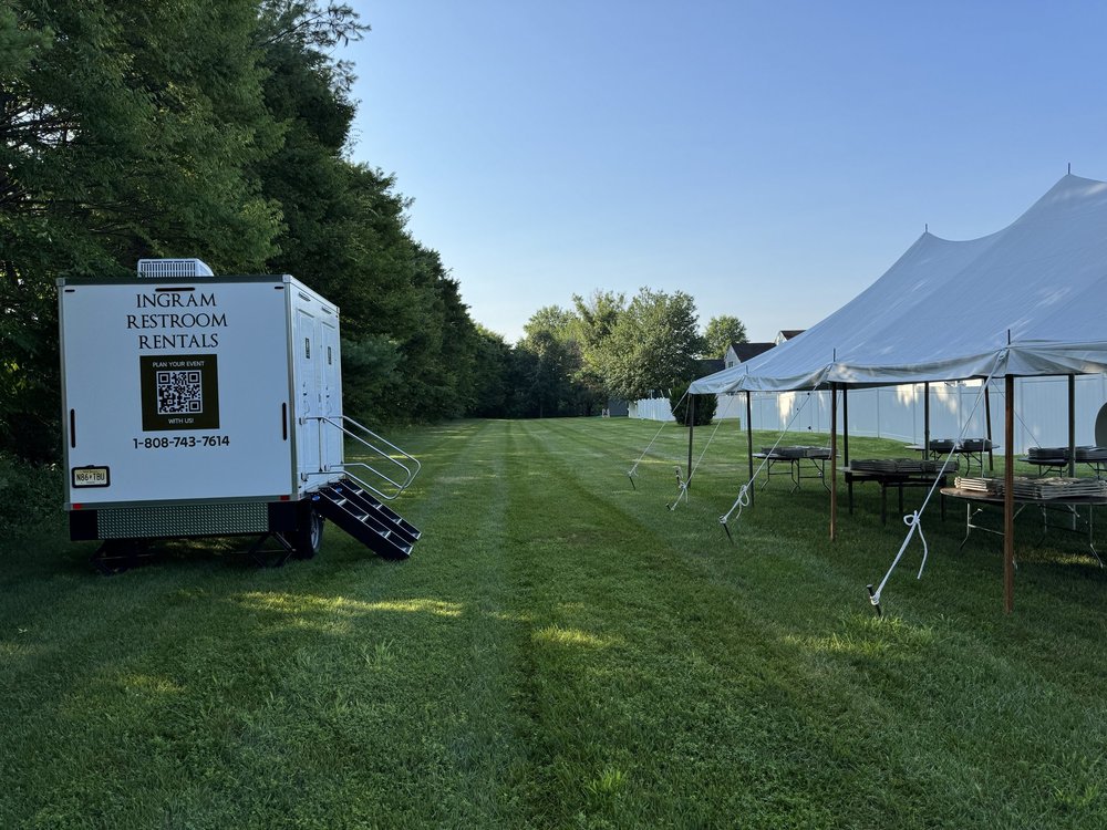 Restroom trailer on a grass field beside an event tent