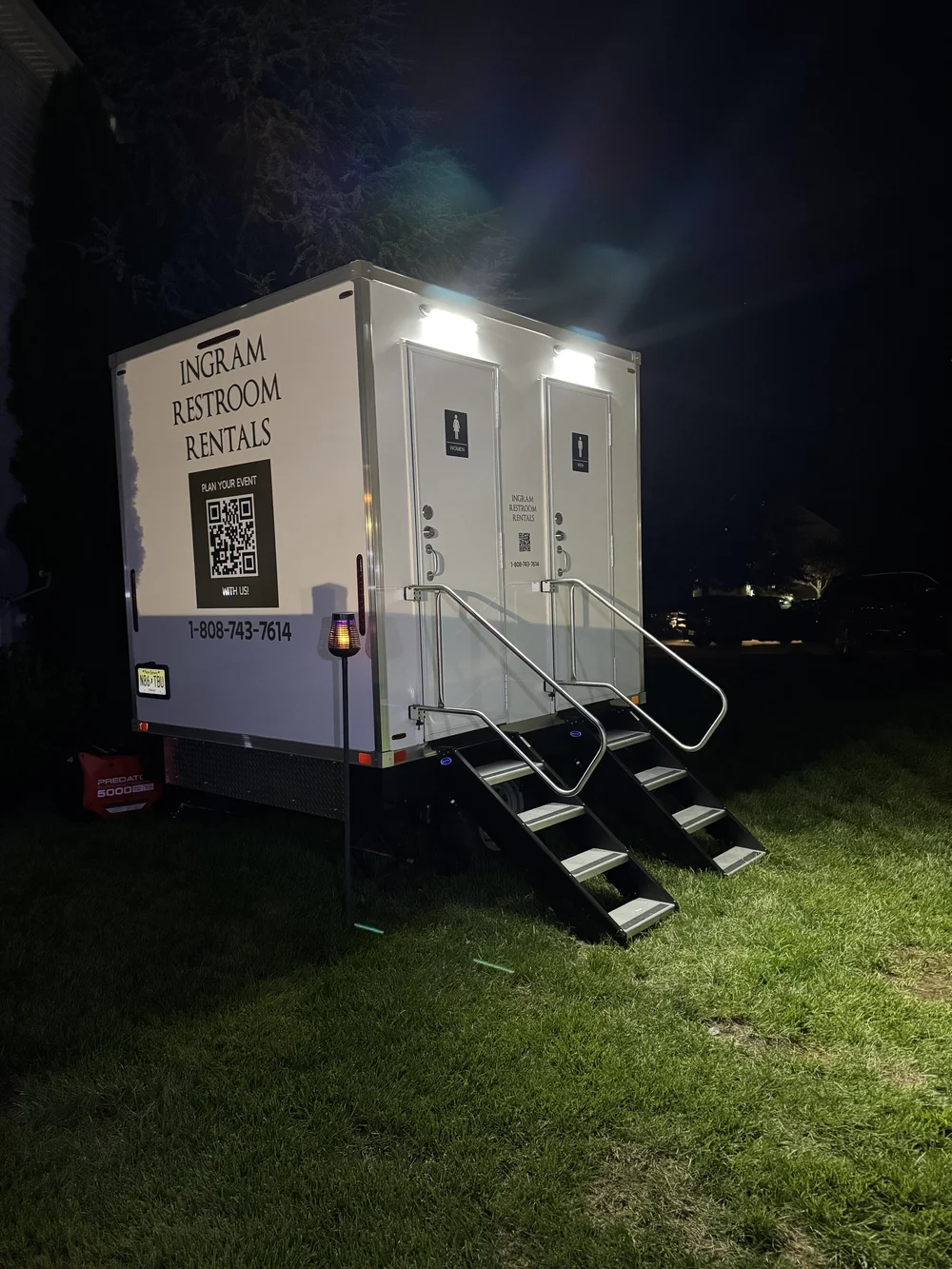 An Ingram restroom trailer glowing at night with steps lit