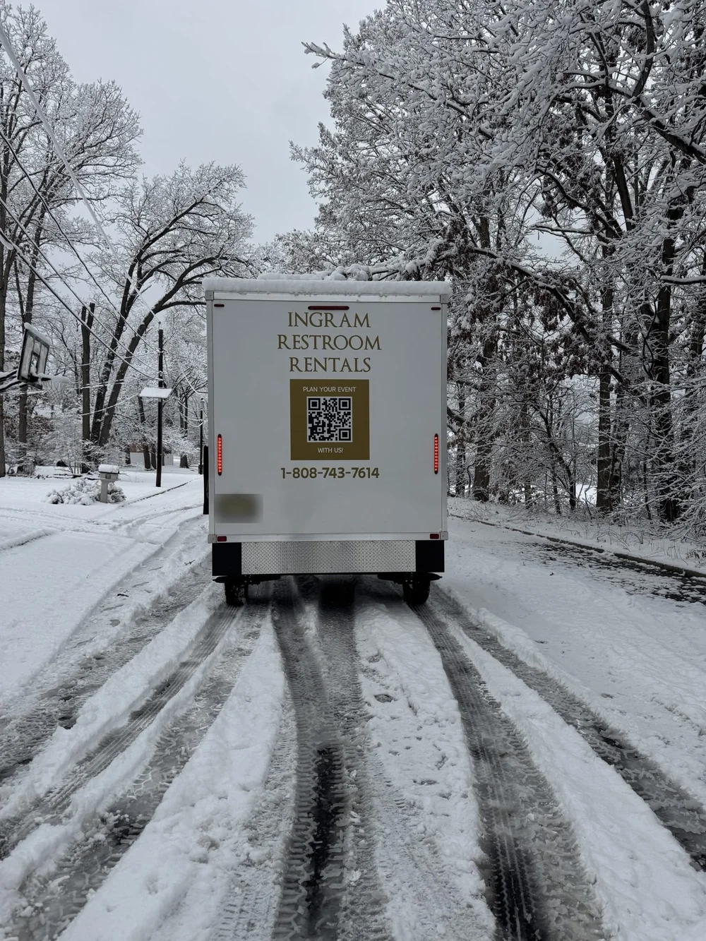 An Ingram restroom trailer being towed down a snowy tree-lined road