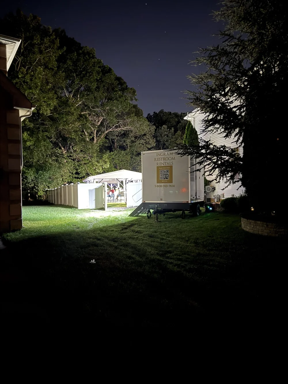 Tráiler de baños iluminado de noche en una fiesta en el patio