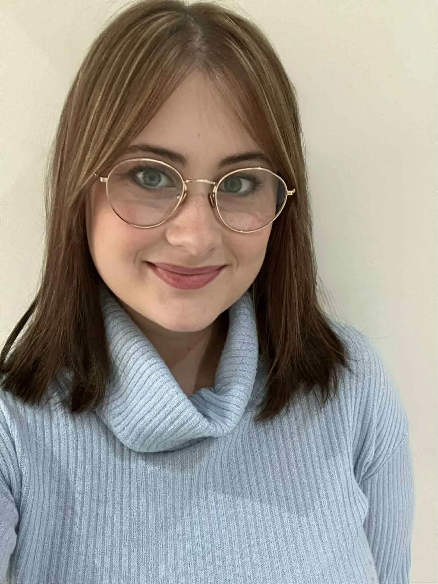 A woman with light brown hair wearing glasses and a light gray turtleneck sweater, smiling at the camera.