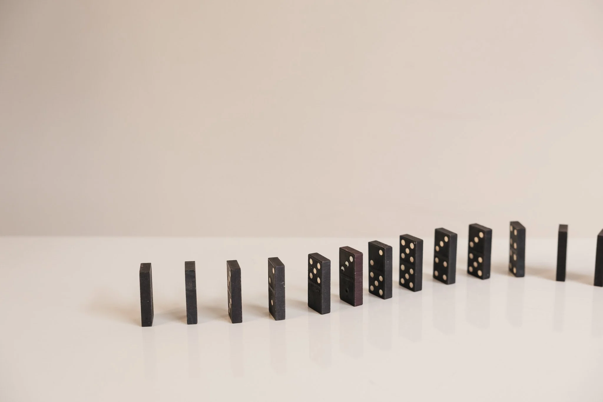 Black dominoes laid out in a line on a white surface, with some toppled over and others standing upright.