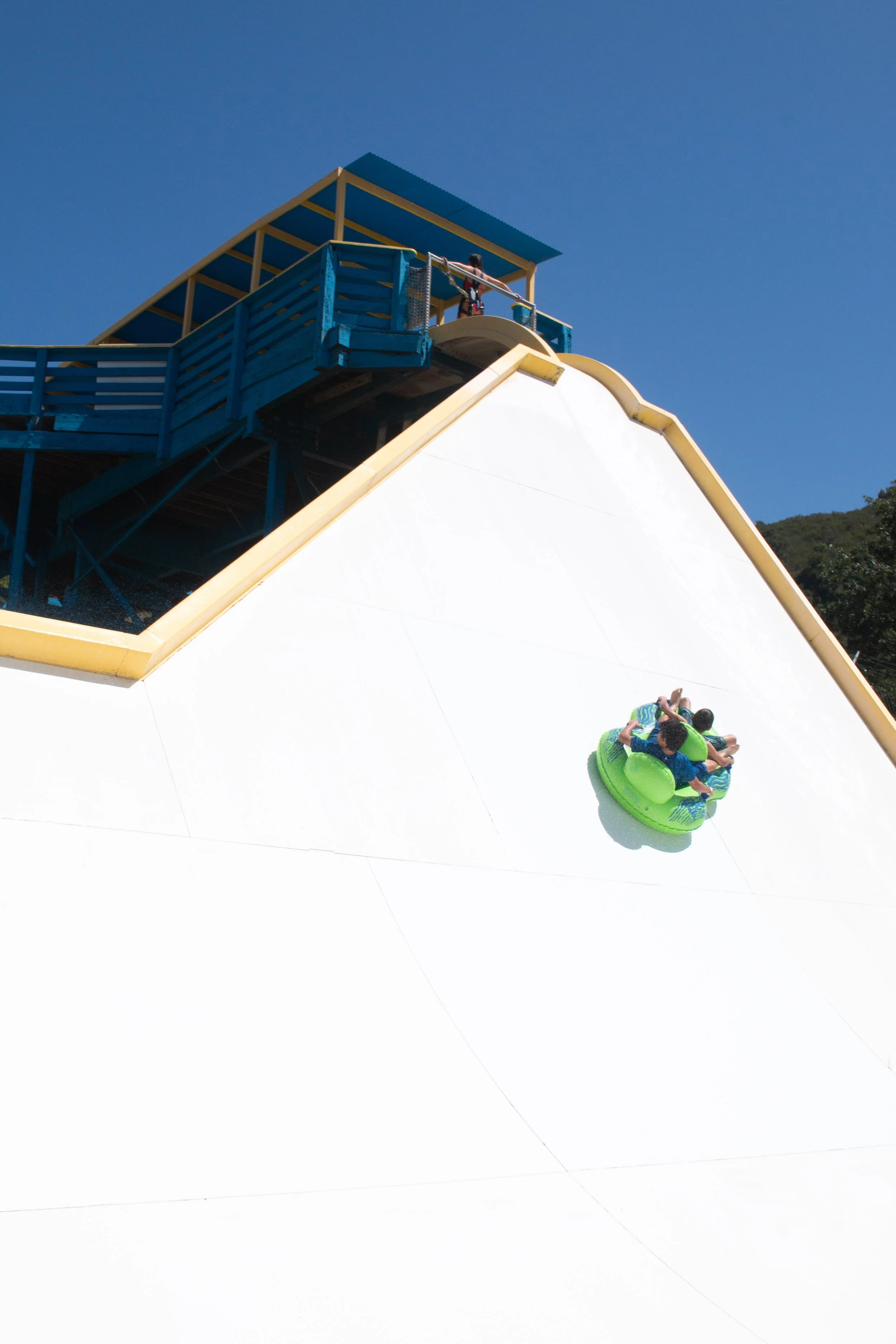 People riding a large water slide, with one person sliding down in a green inner tube on the Stampede at Mustang Waterpark and others at the top ready to slide down.