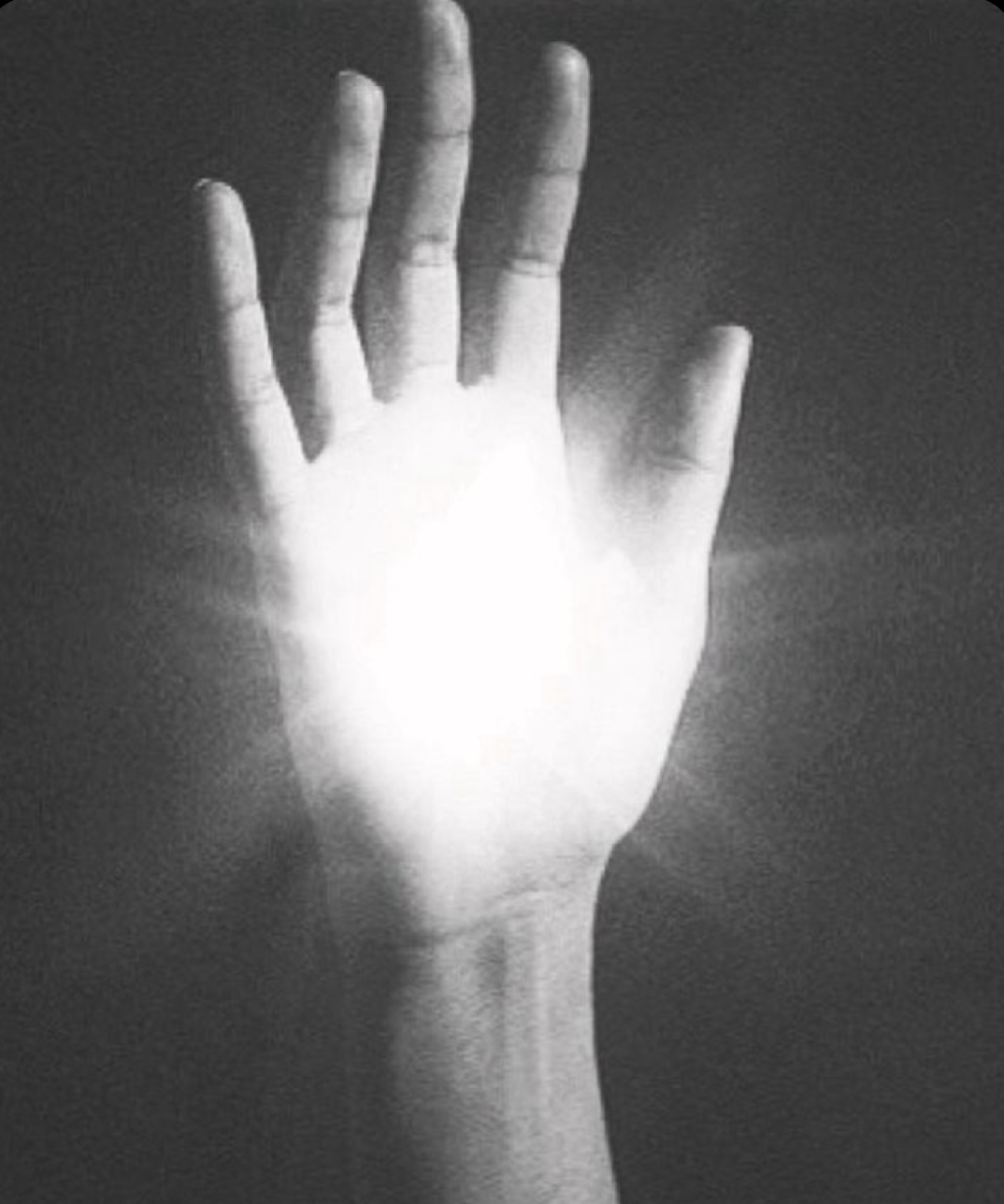 Black and white image of a hand with a glowing or illuminated palm, raised vertically against a dark background.