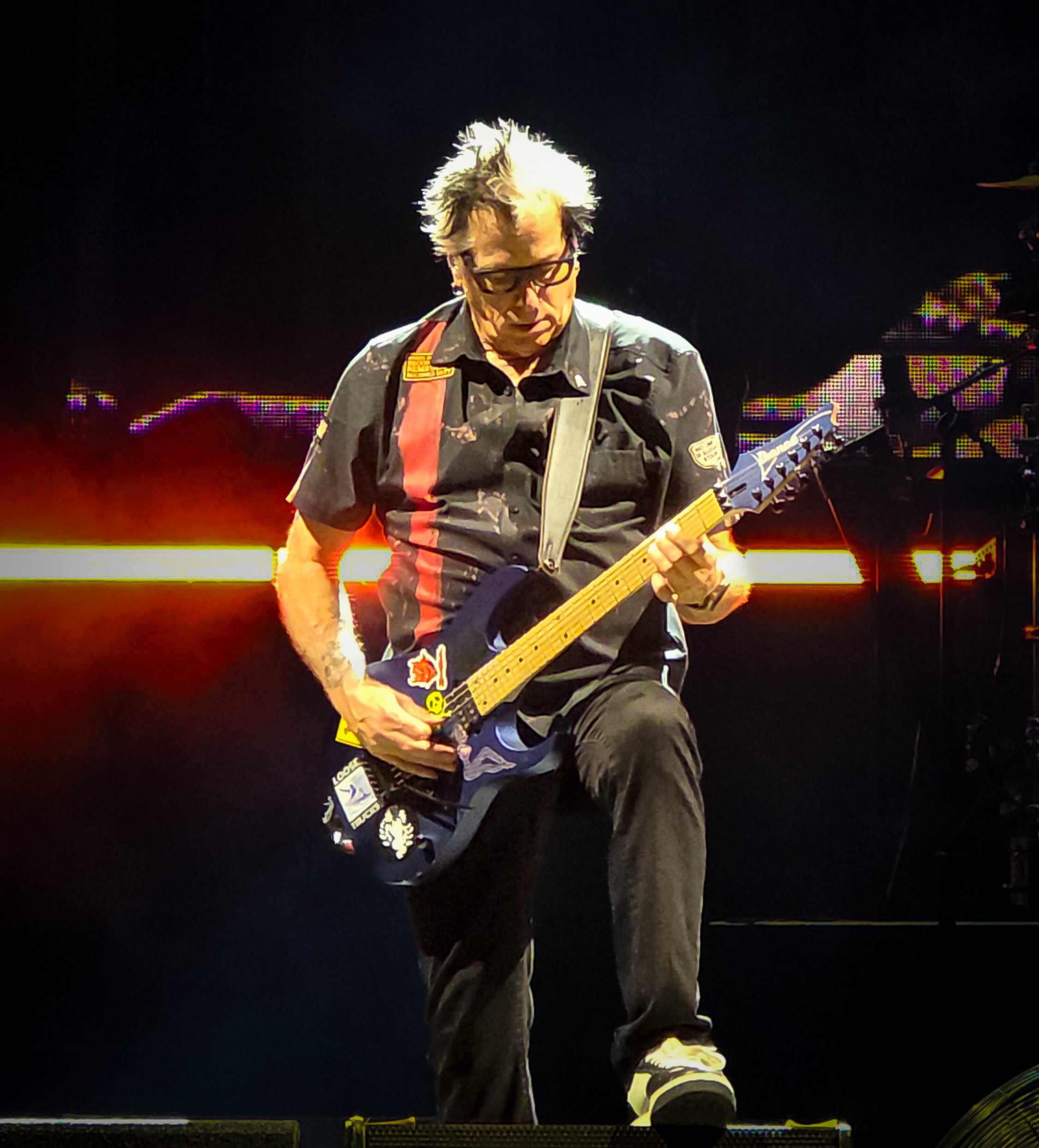 A musician playing an electric guitar on stage with colorful lighting and a dark background.