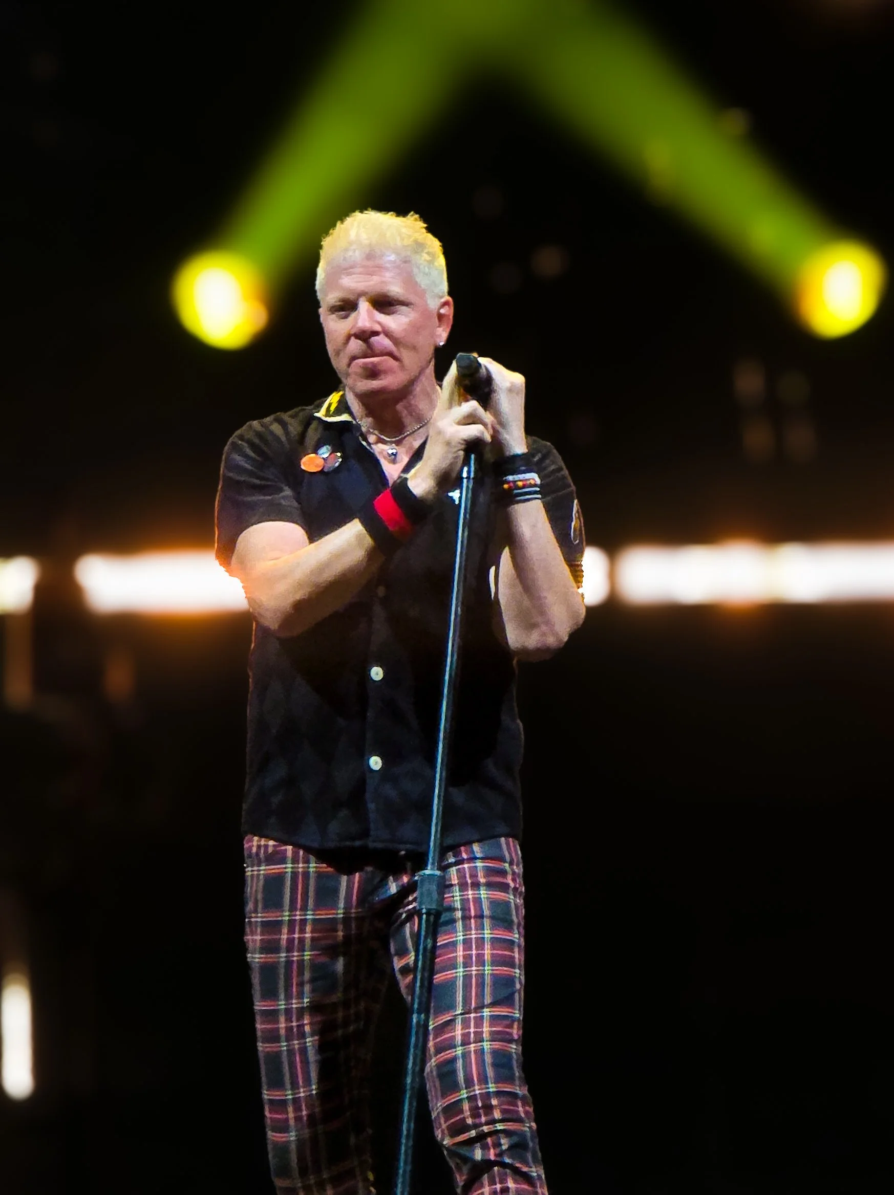 A blonde male singer holding a microphone on stage with yellow stage lights in the background.