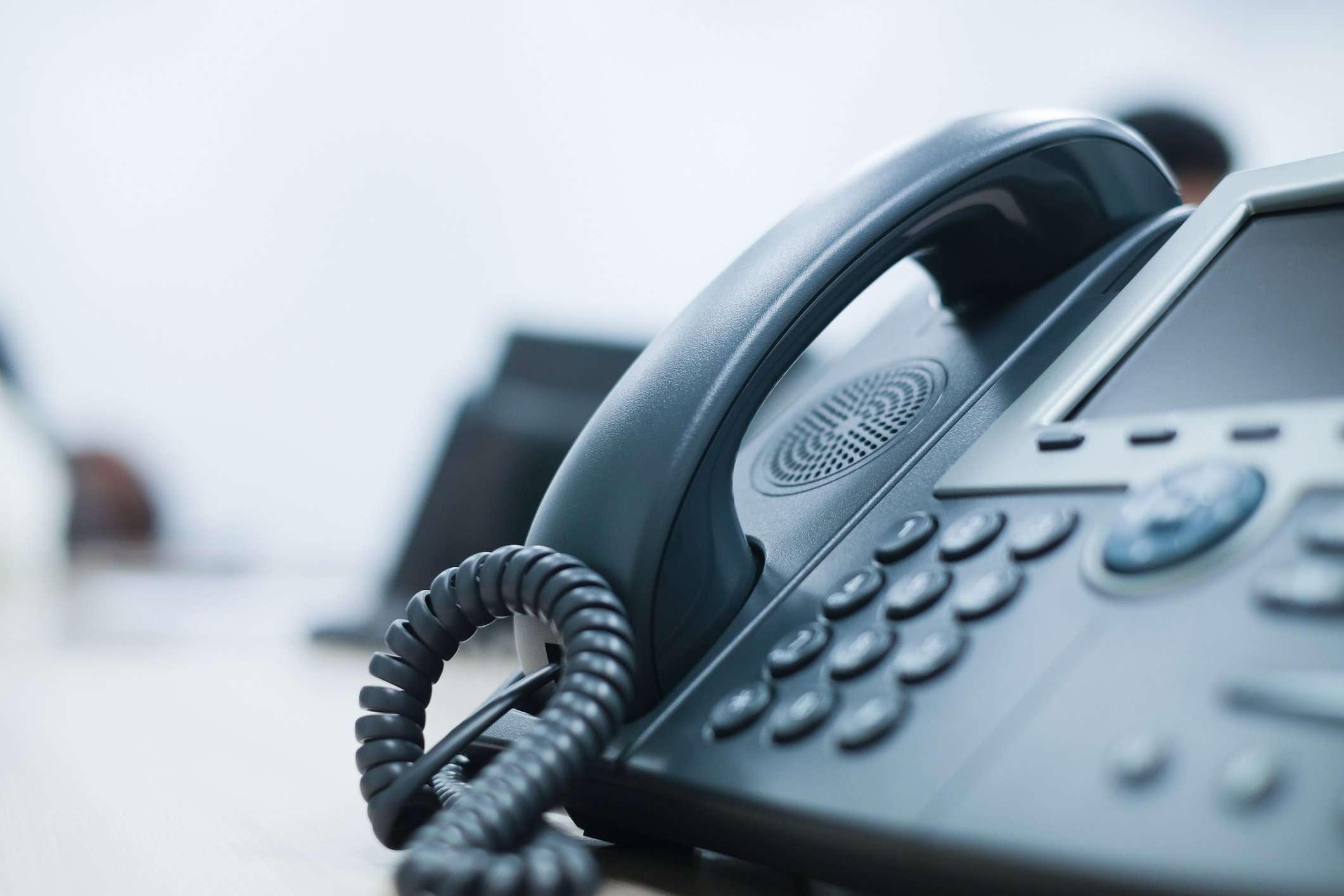 Close-up of a black office telephone with a corded handset on a white desk.
