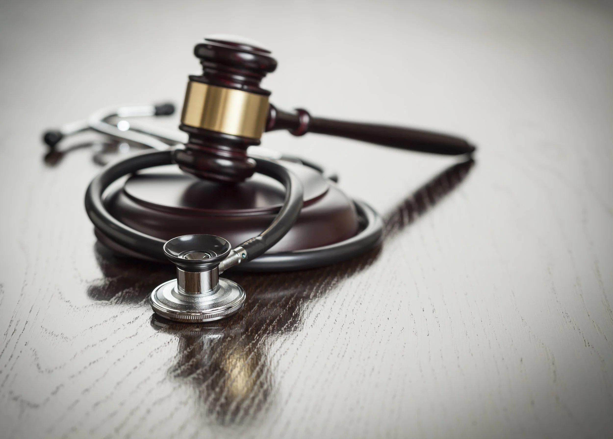A wooden gavel and a stethoscope on a light-colored wooden surface.