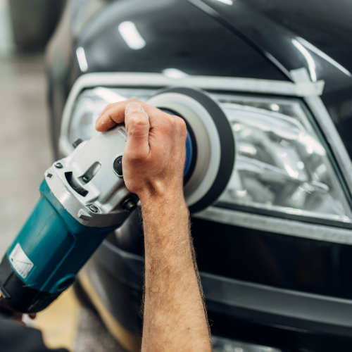 Person polishing a black car's headlight with a handheld polishing tool.