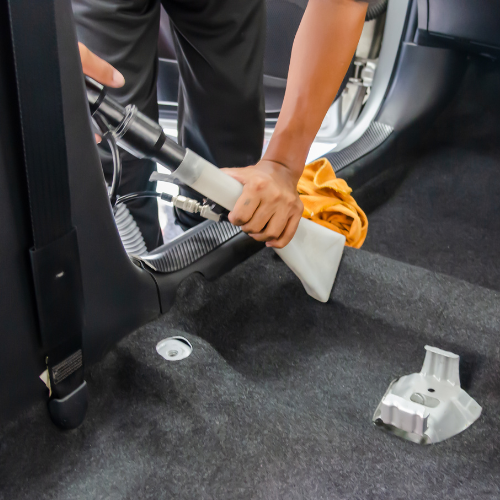 Person using a handheld cleaning tool to vacuum the interior floor of a vehicle.