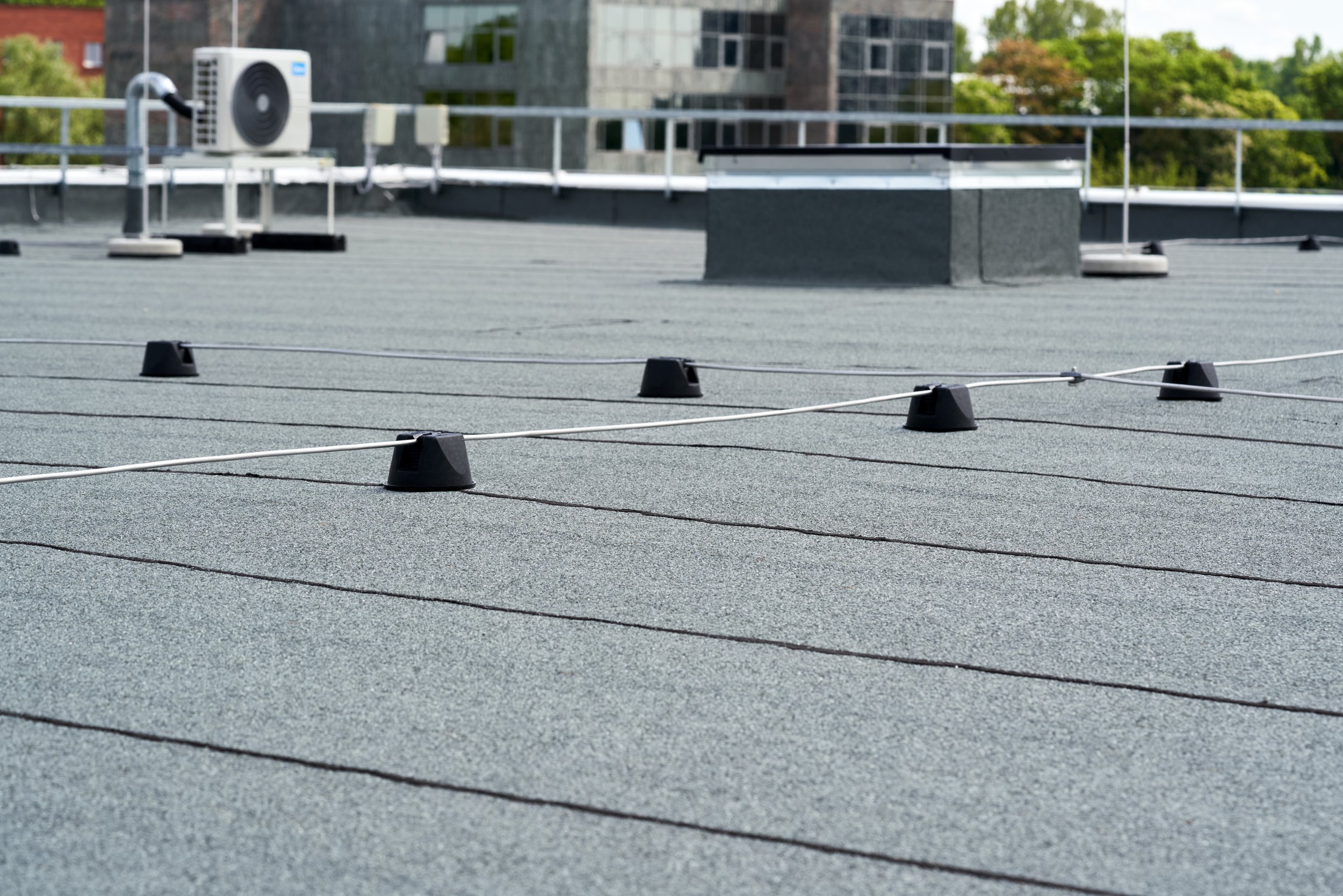 Rooftop with surface mounted wires and vents, city buildings and green trees in the background.