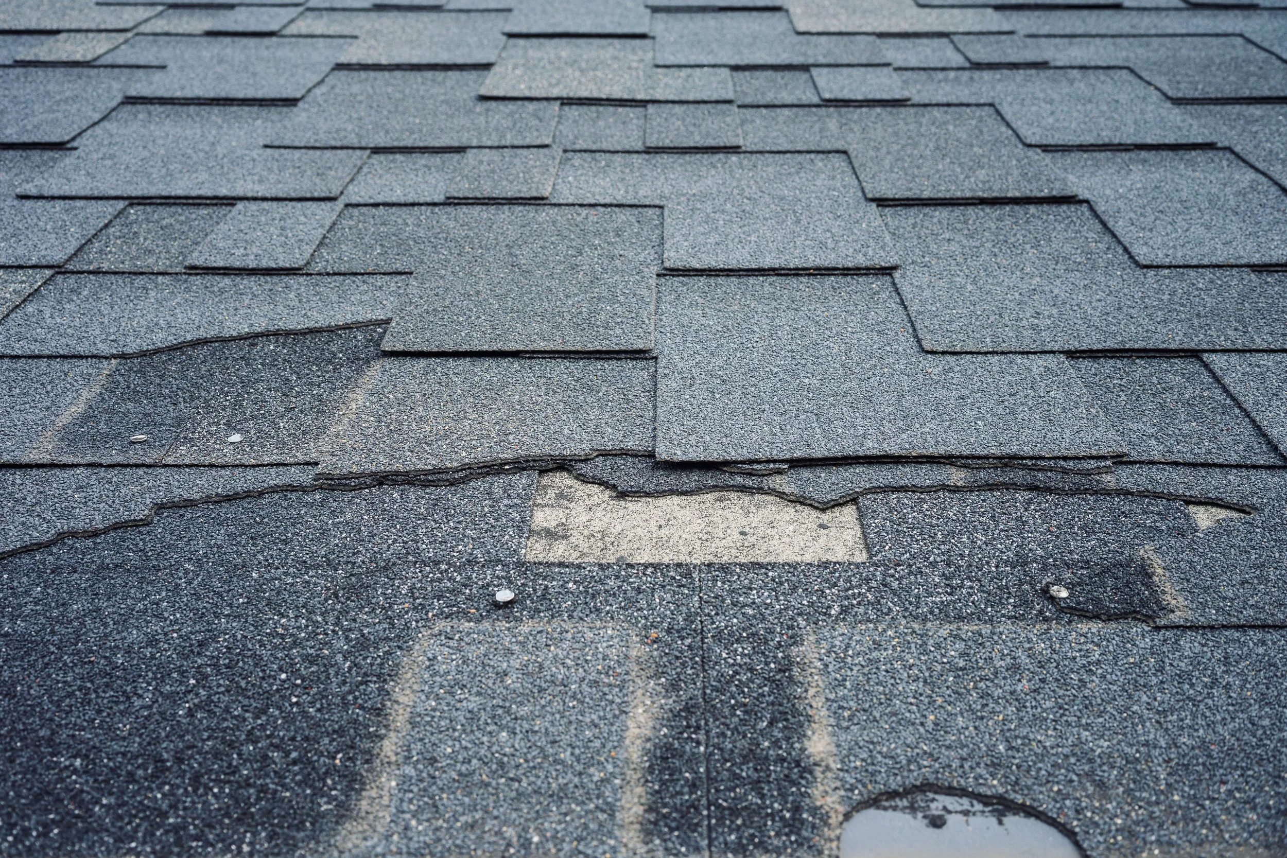 Close-up of a roof with asphalt shingles, showing a damaged section with missing shingles and exposed underlying surface.