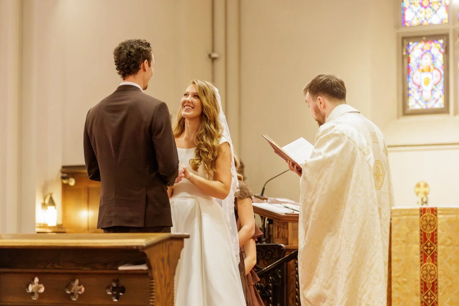 A couple looking at each other and getting married, with a priest reading prayers from a book.