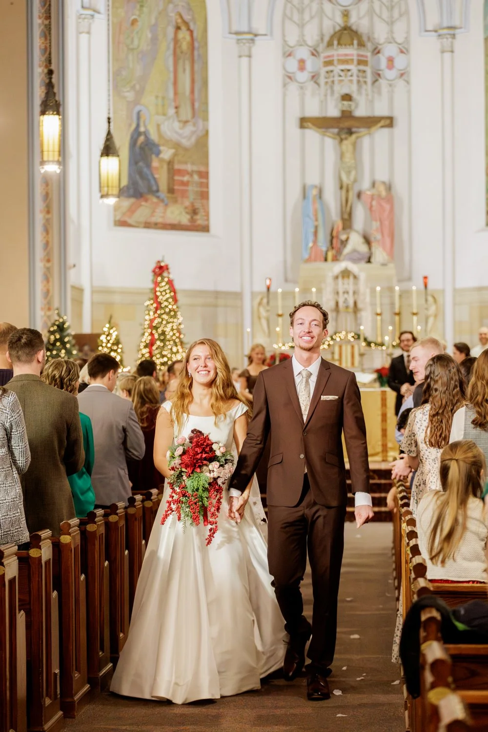 A bride and groom walking down the aisle, surrounded by guests, with Christmas decorations and an altar in the background.