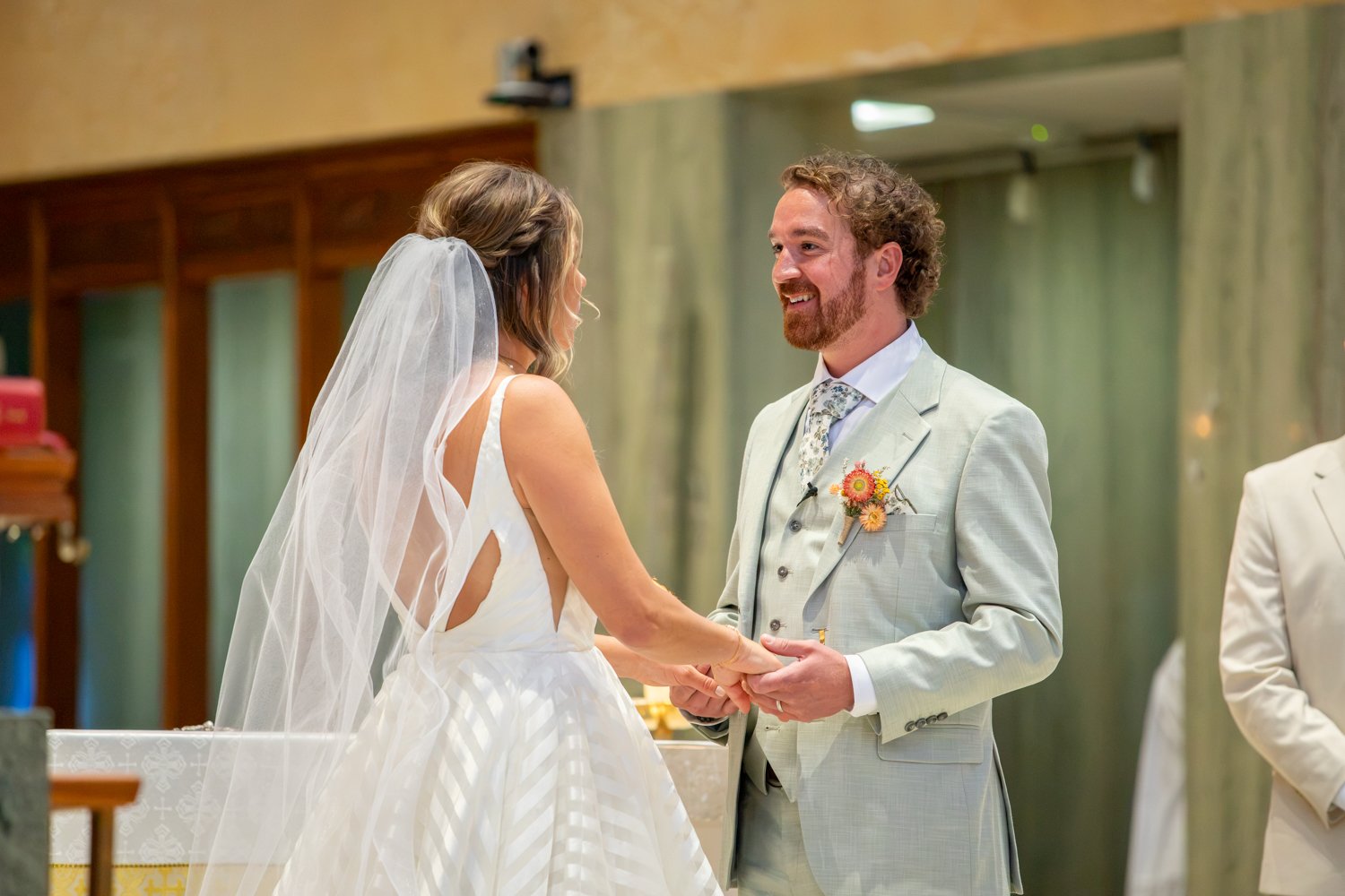 A bride and groom holding hands and smiling during their wedding ceremony.