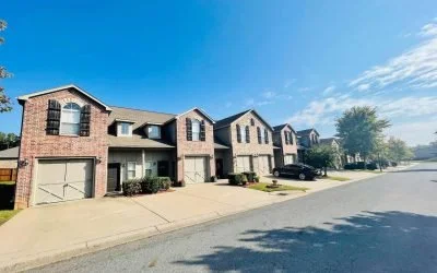 Row of attached townhouses with garages, parked cars, and a clear blue sky.