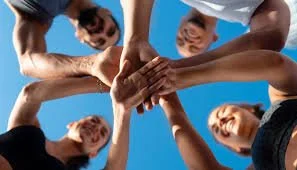 Group of diverse people putting hands together in a team huddle against a blue sky.
