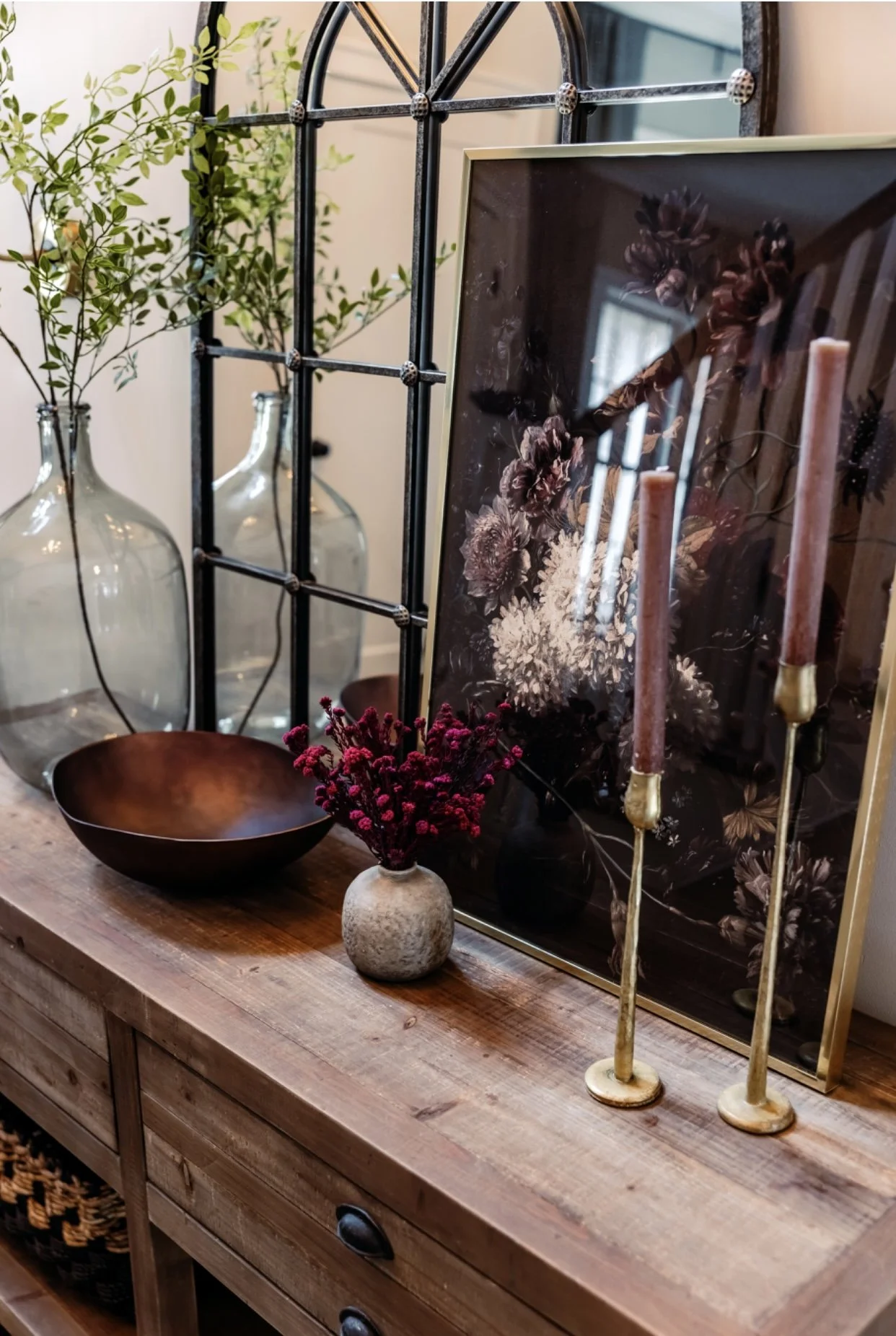 entryway console table with framed art, candlesticks, bowl, and a vase with stems 