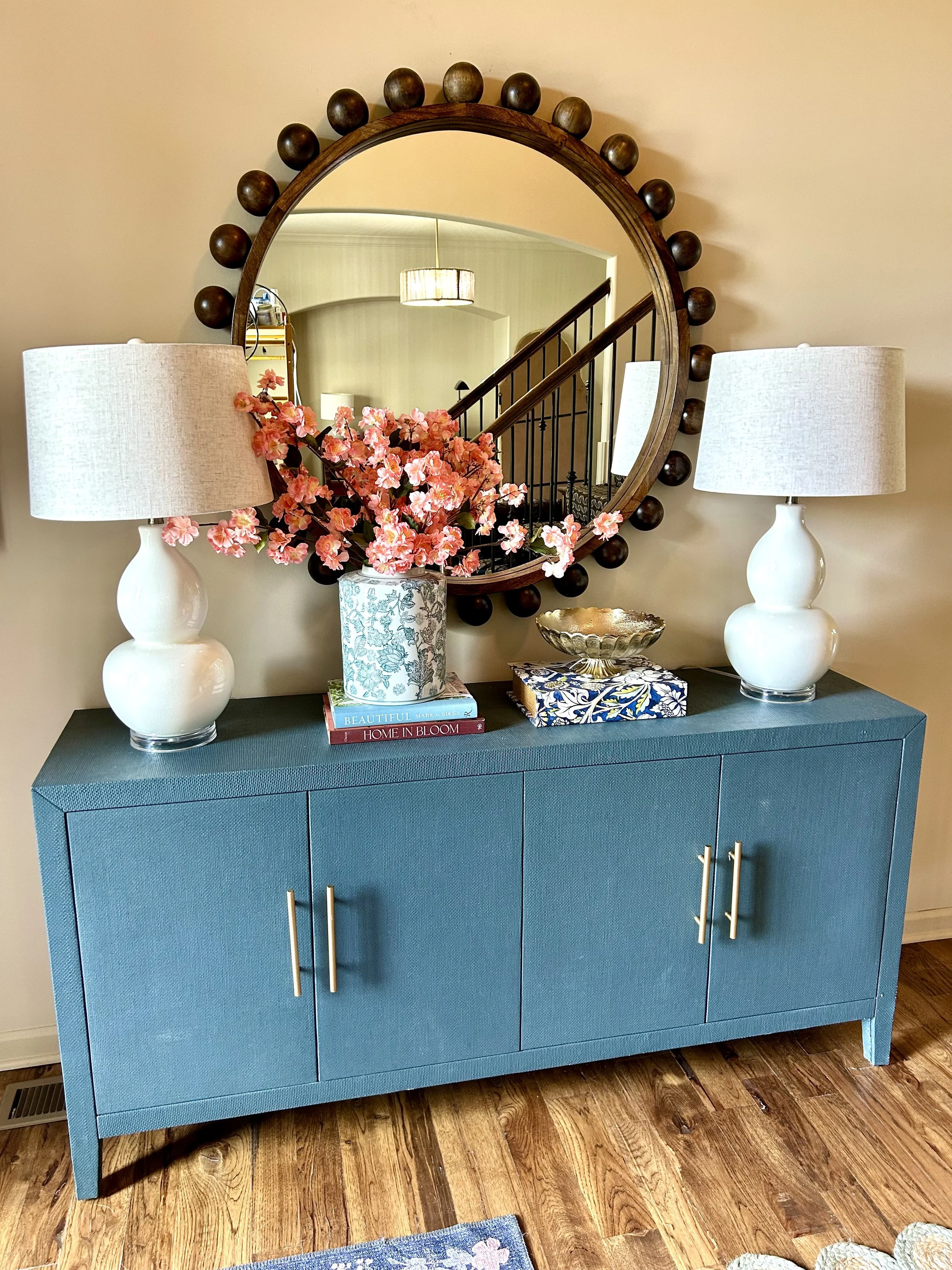 blue console table with two white lamps, a vase of flowers and unique wall mirror