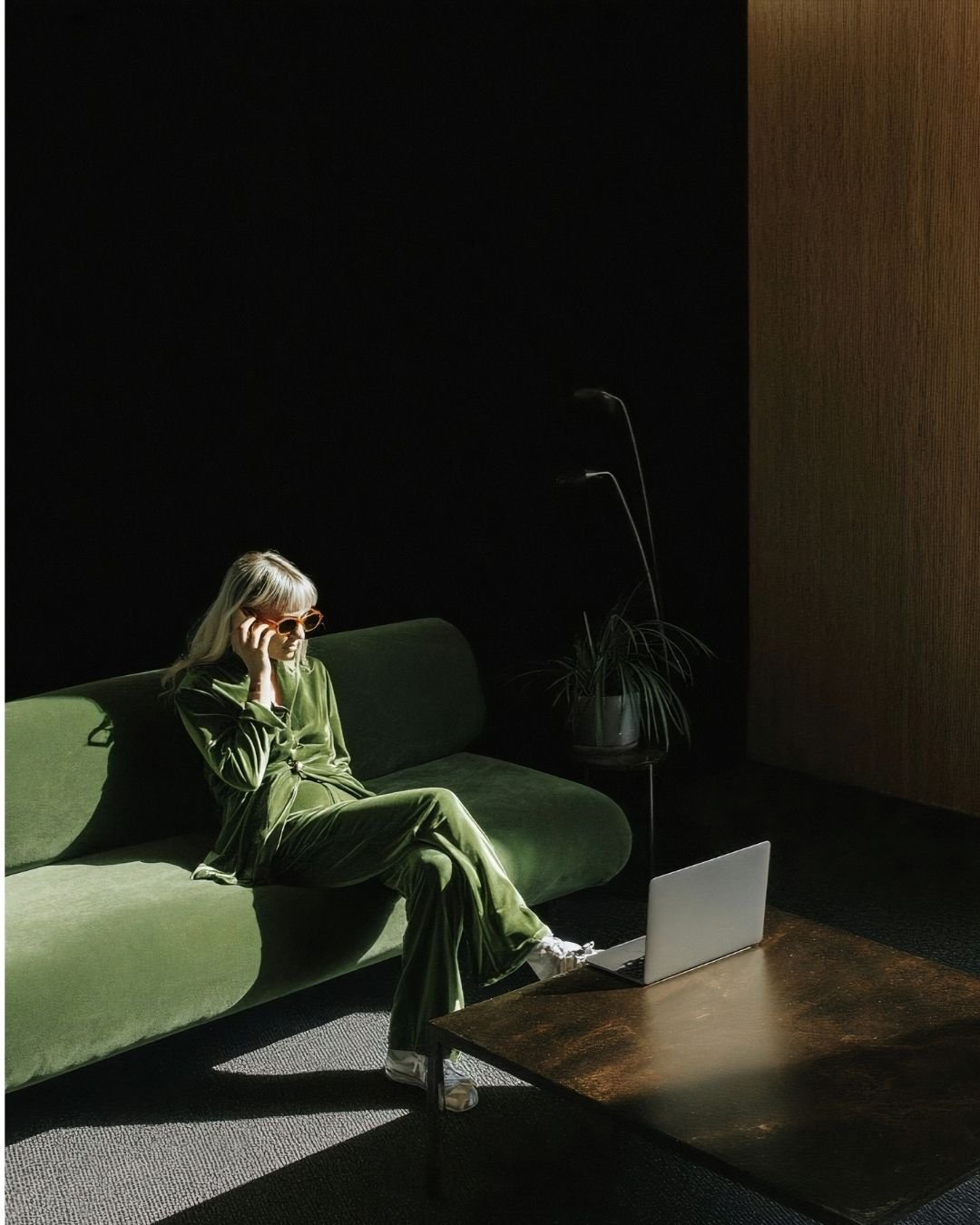 Women sitting on a velvet couch in a velvet suit talking on the phone, legs crossed.
