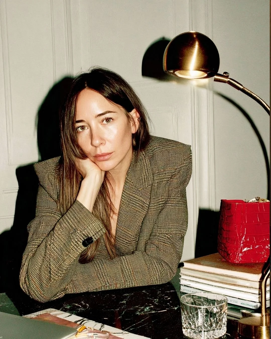 Women staring into the camera leaning on her arm at a desk