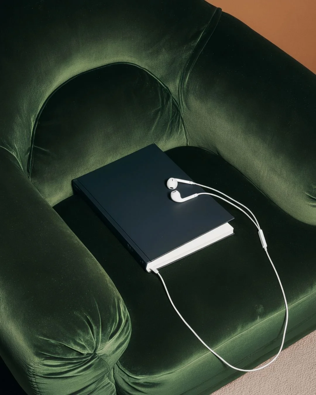 A book and headphones on a green velvet chair