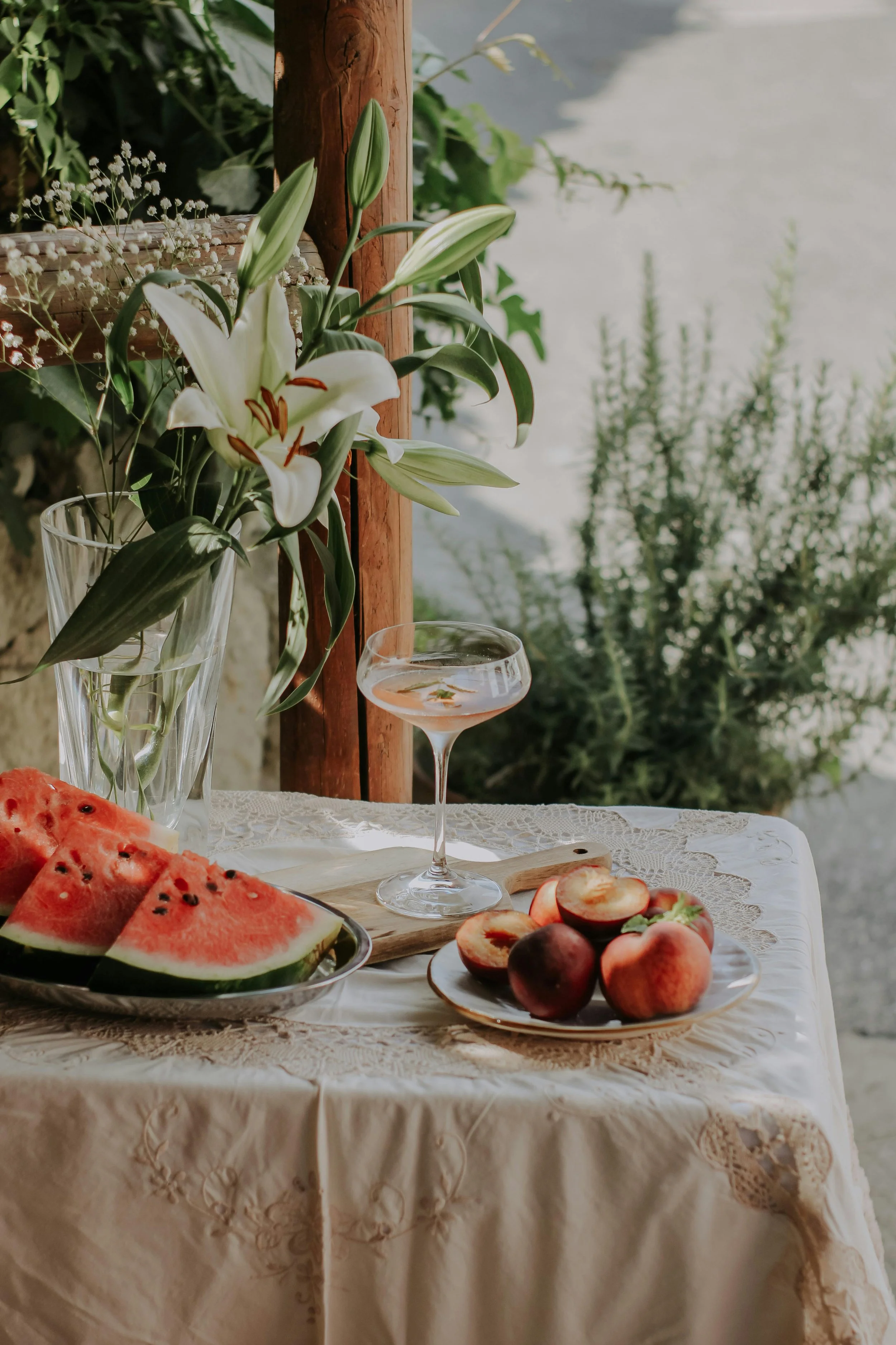 Dining table with a half-filled champagne glass, surrounded by peach and watermelon and a floral centerpiece