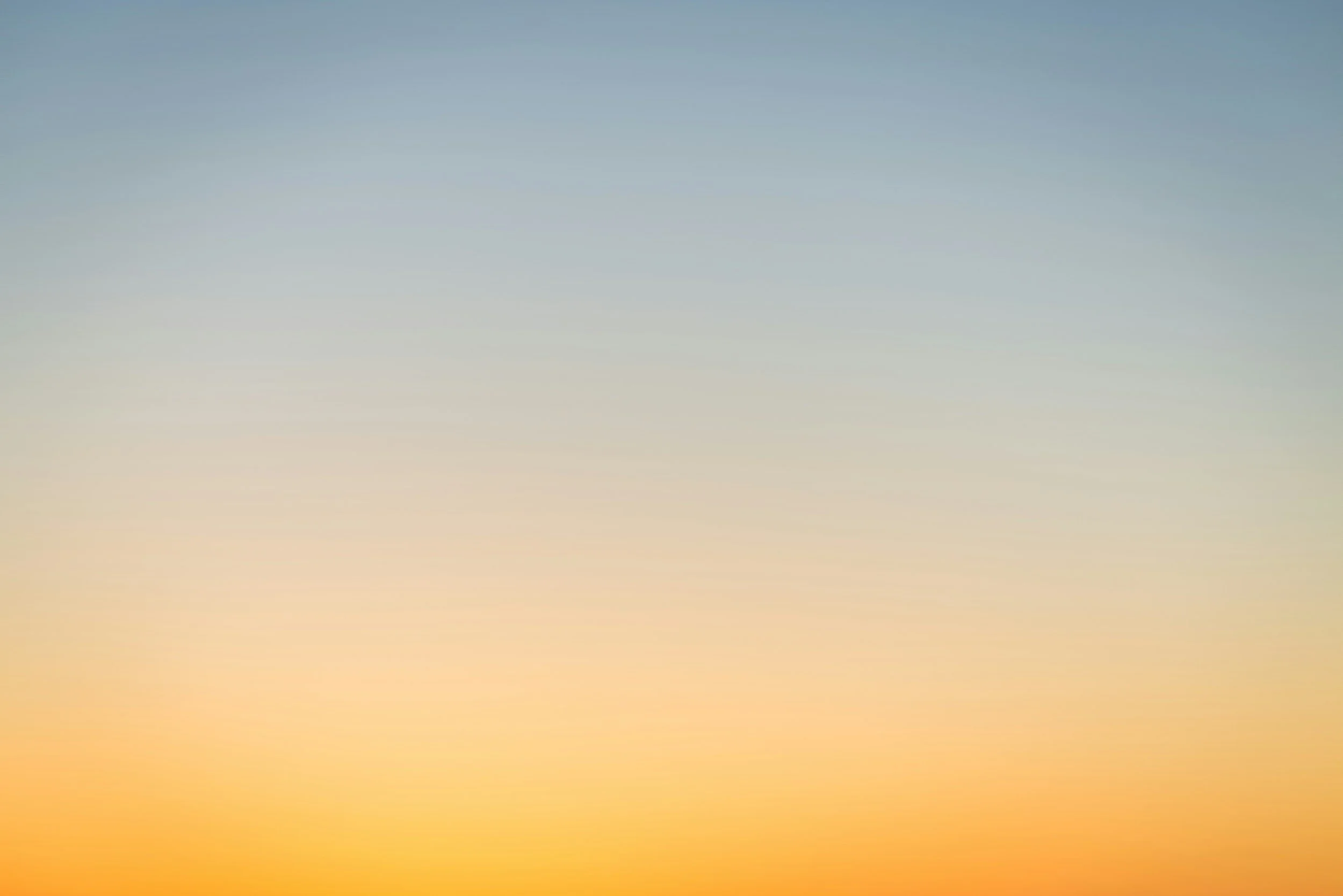 Blurred gradient sky at sunset or sunrise with shades of blue, orange, and yellow.