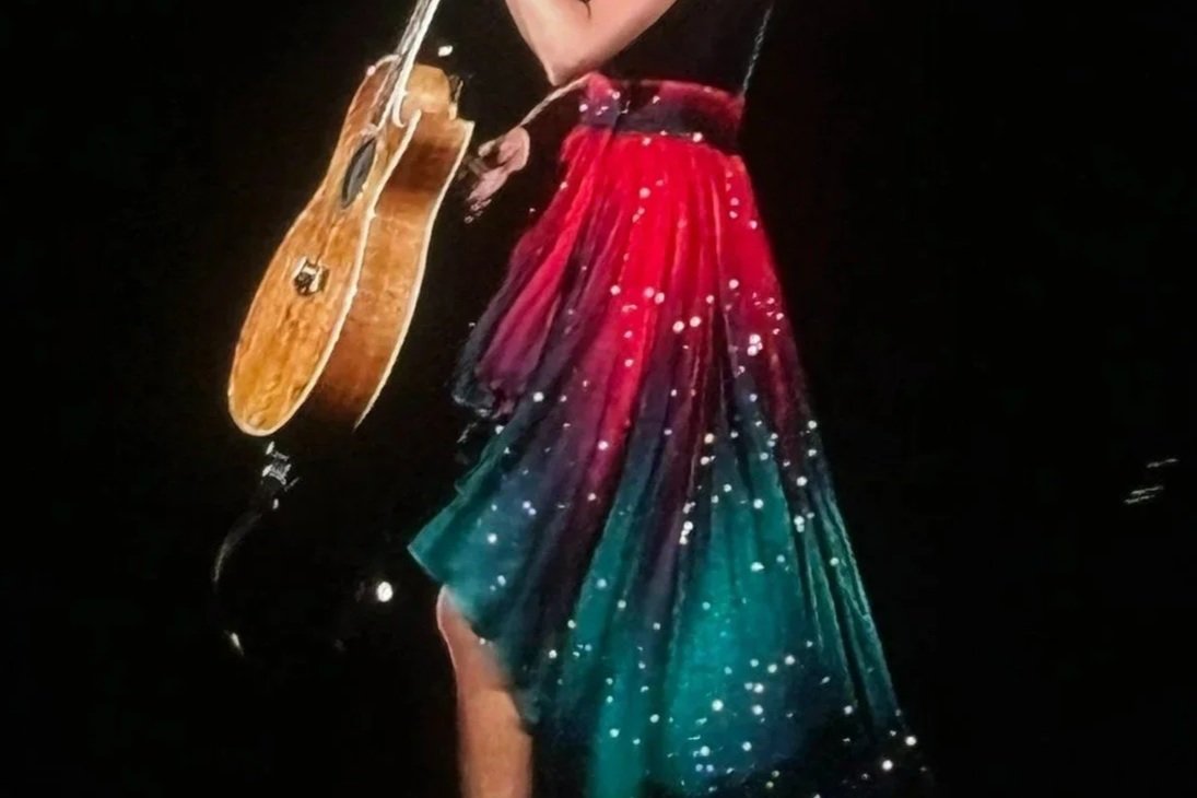 A person in a colorful, galaxy-patterned dress carrying a guitar.