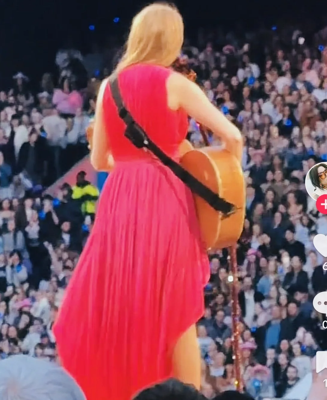 Back view of a woman in a red dress playing guitar on stage in front of a large seated audience.