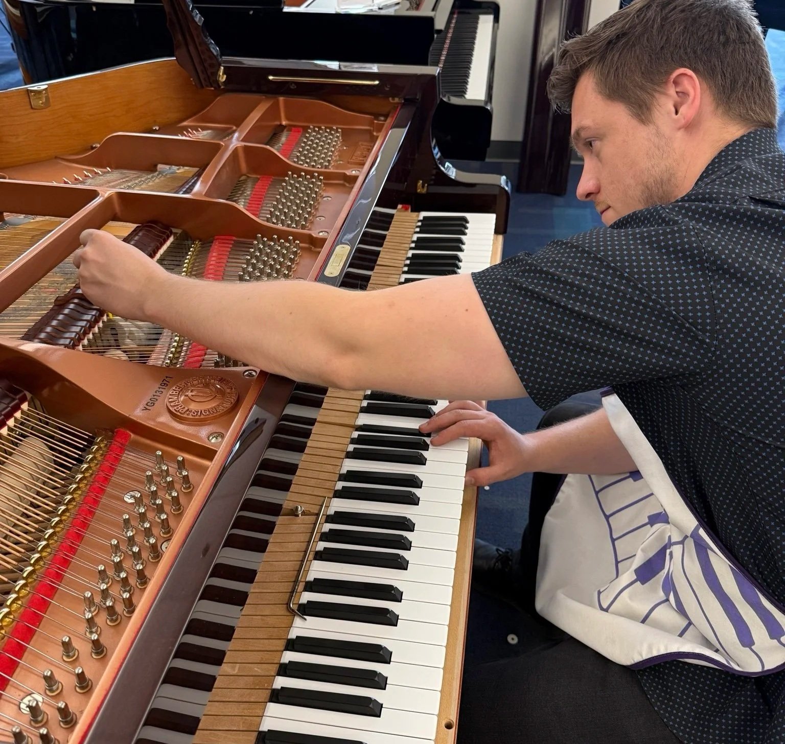 A man regulating an upright grand piano, with focus on his hands and face as he presses the piano keys.