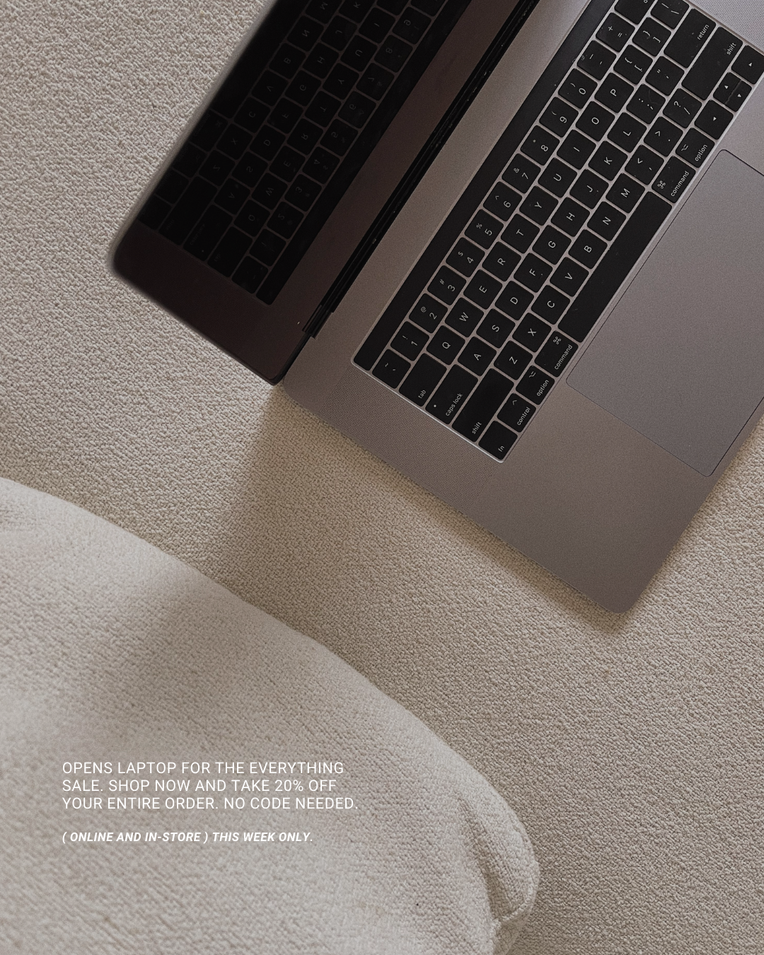 A silver laptop with black keyboard resting on a beige fabric surface, with promotional text for a sale.