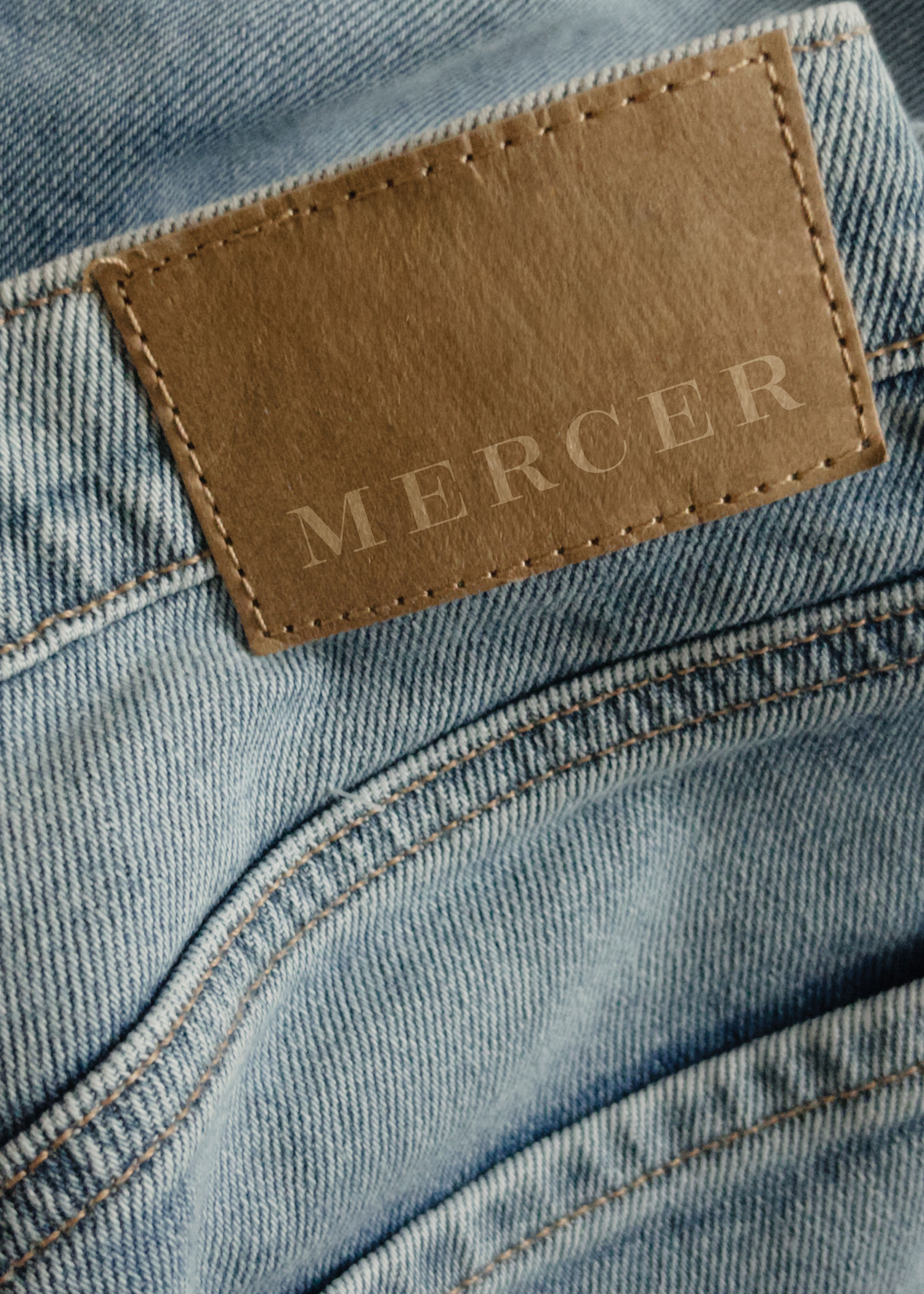 Close-up of the back pocket of blue jeans with a brown leather patch labeled 'MERCER'.