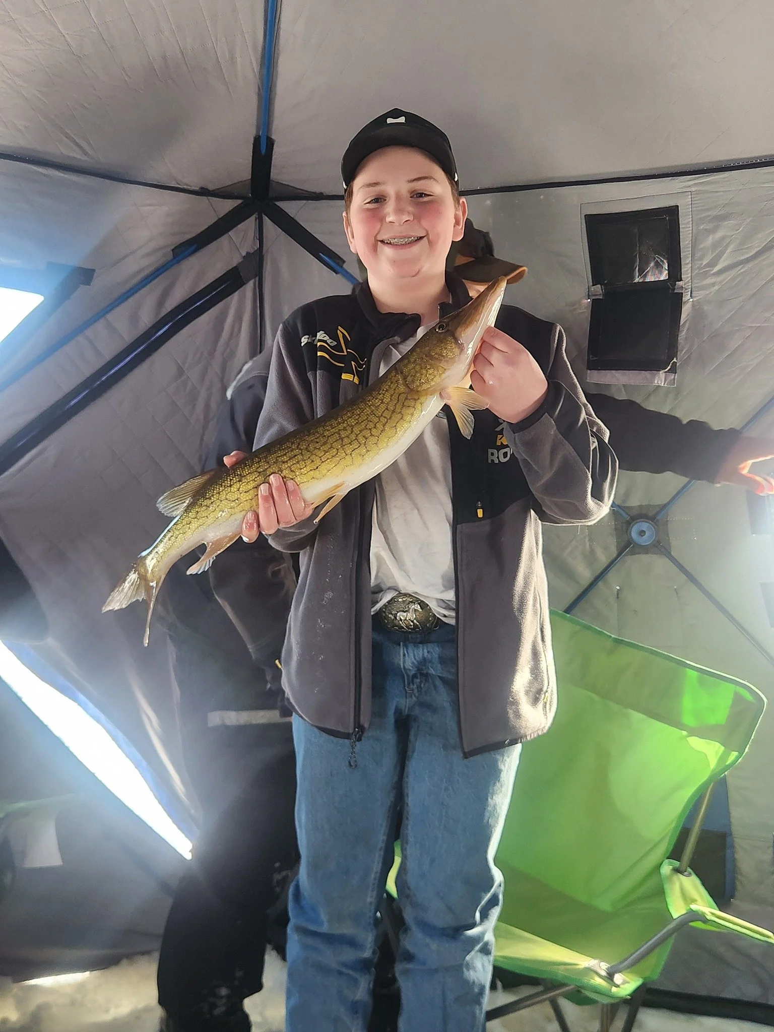 A boy smiling and holding a fish inside a tent