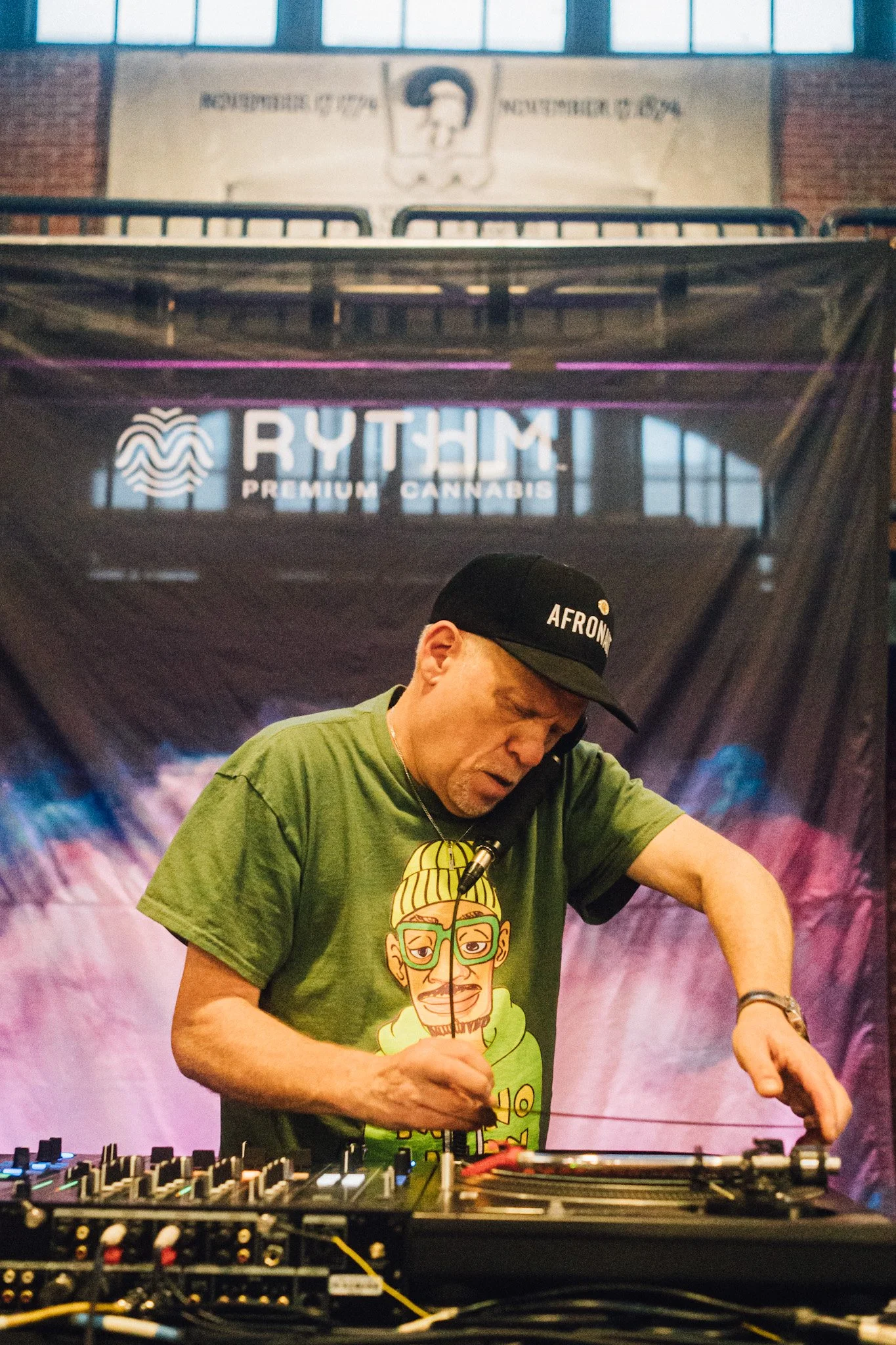 A DJ mixes music at a RYTHM event, with a banner reading 'PREMIUM CANNABIS' in the background.