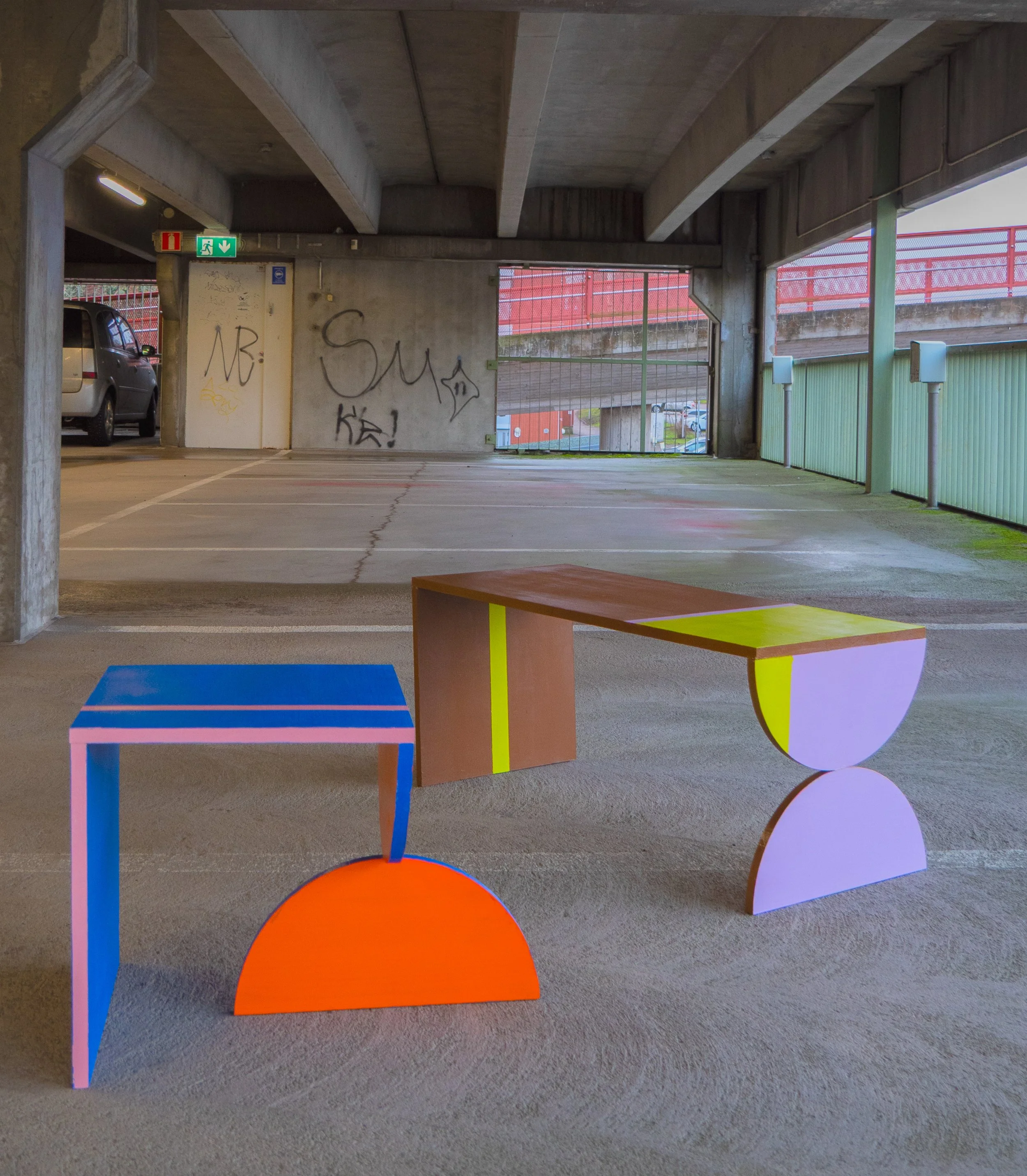 Kaksi modernia, värikkäästi maalattua pöytää pysäköintihallissa.