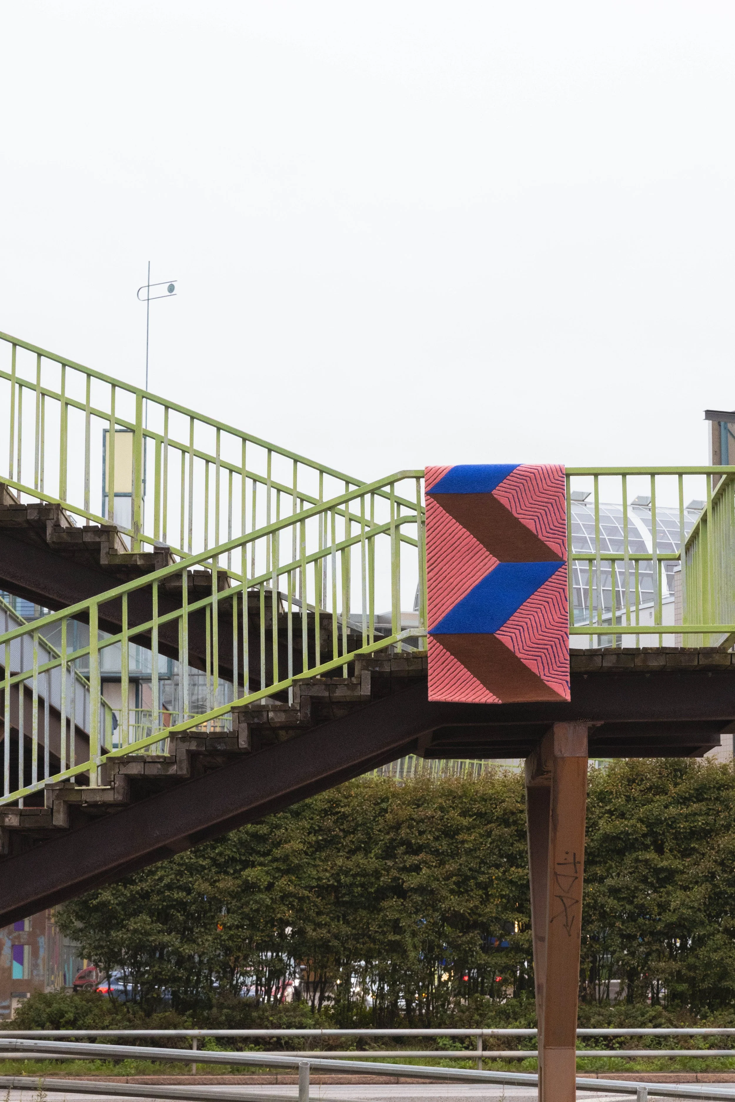 Ulkotakapihoilla oleva vihreä kävelysilta, jossa on matto roikkumassa aidan päällä.